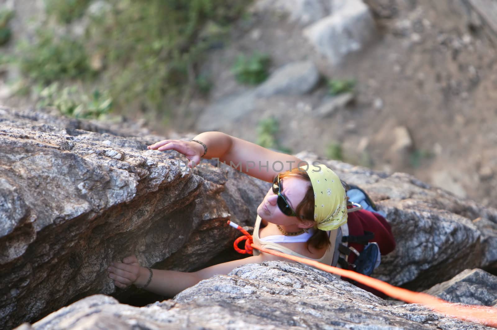A young woman climbs a crack in the rock. She is secured by top rope belay.