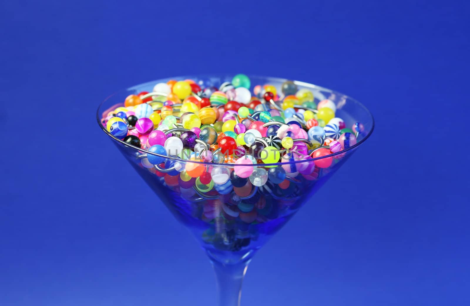 A martini glass full of navel rings. On Saturated Blue Background