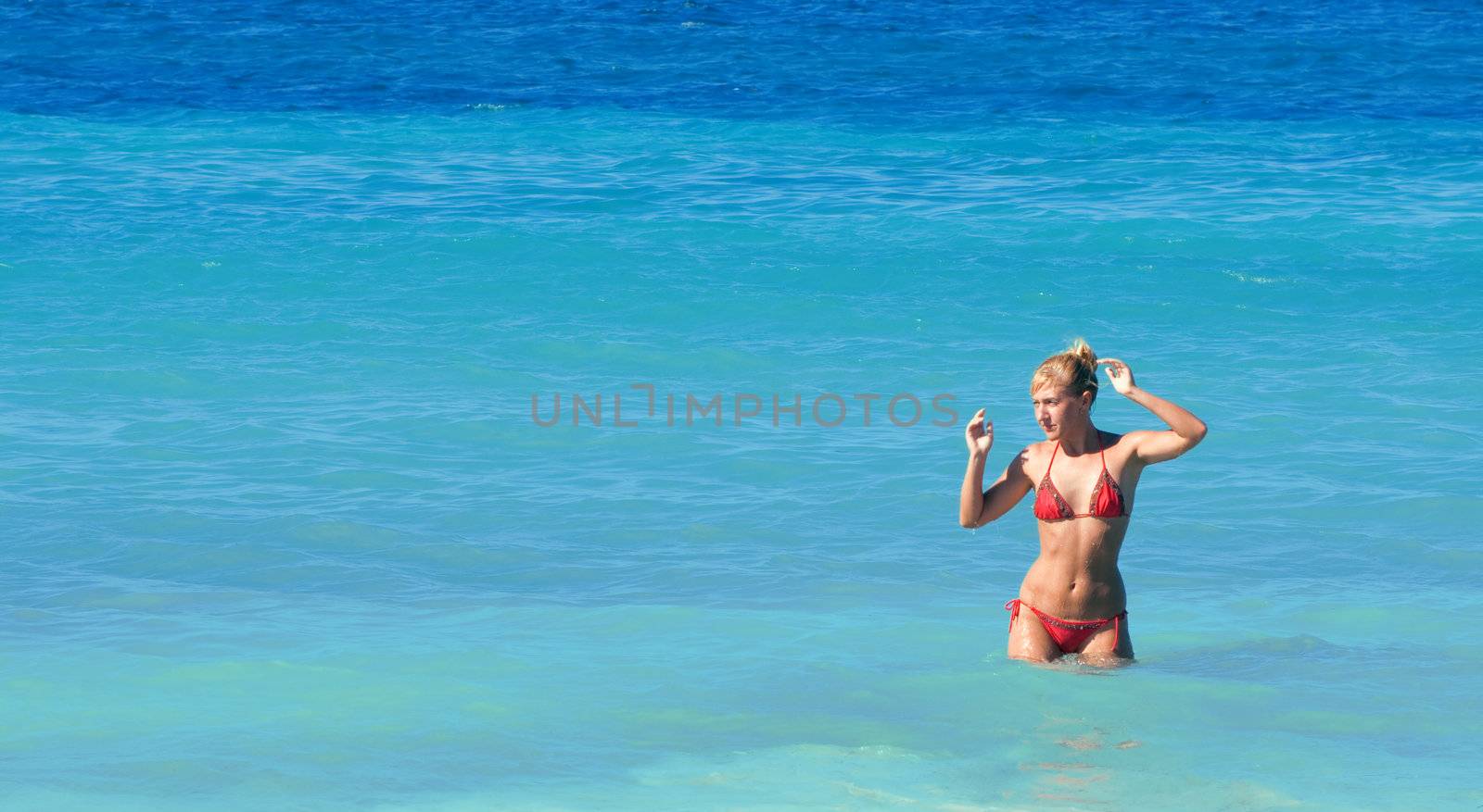 Sexy woman in red bikini posing in a blue sea