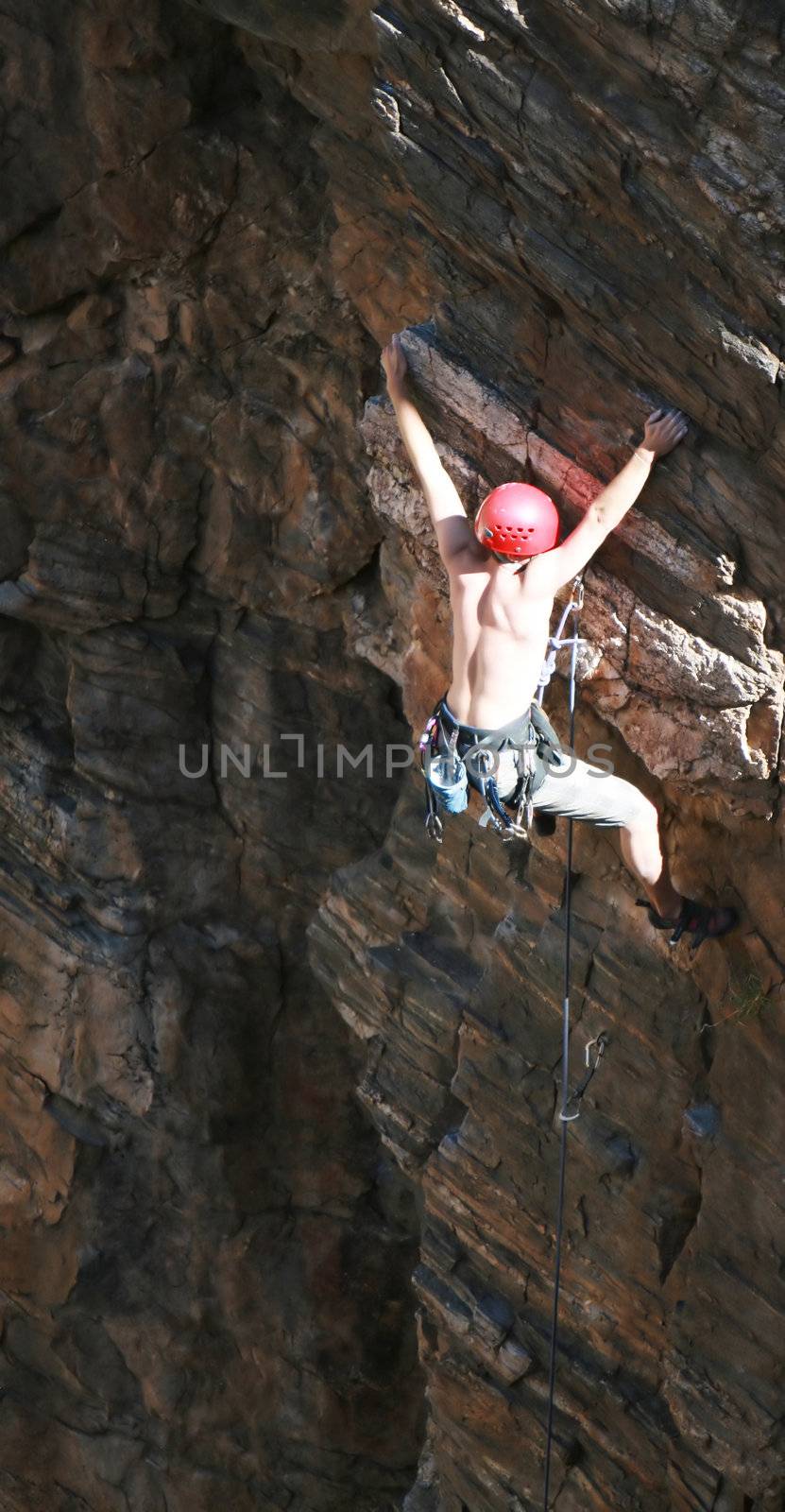 A rock climber works his way up a rock face protected by a rope clipped into bolts. He is wearing a helmet and quickdraws dangle from his harness. The route is in the desert southwest United States. Mt Lemmon, Arizona.