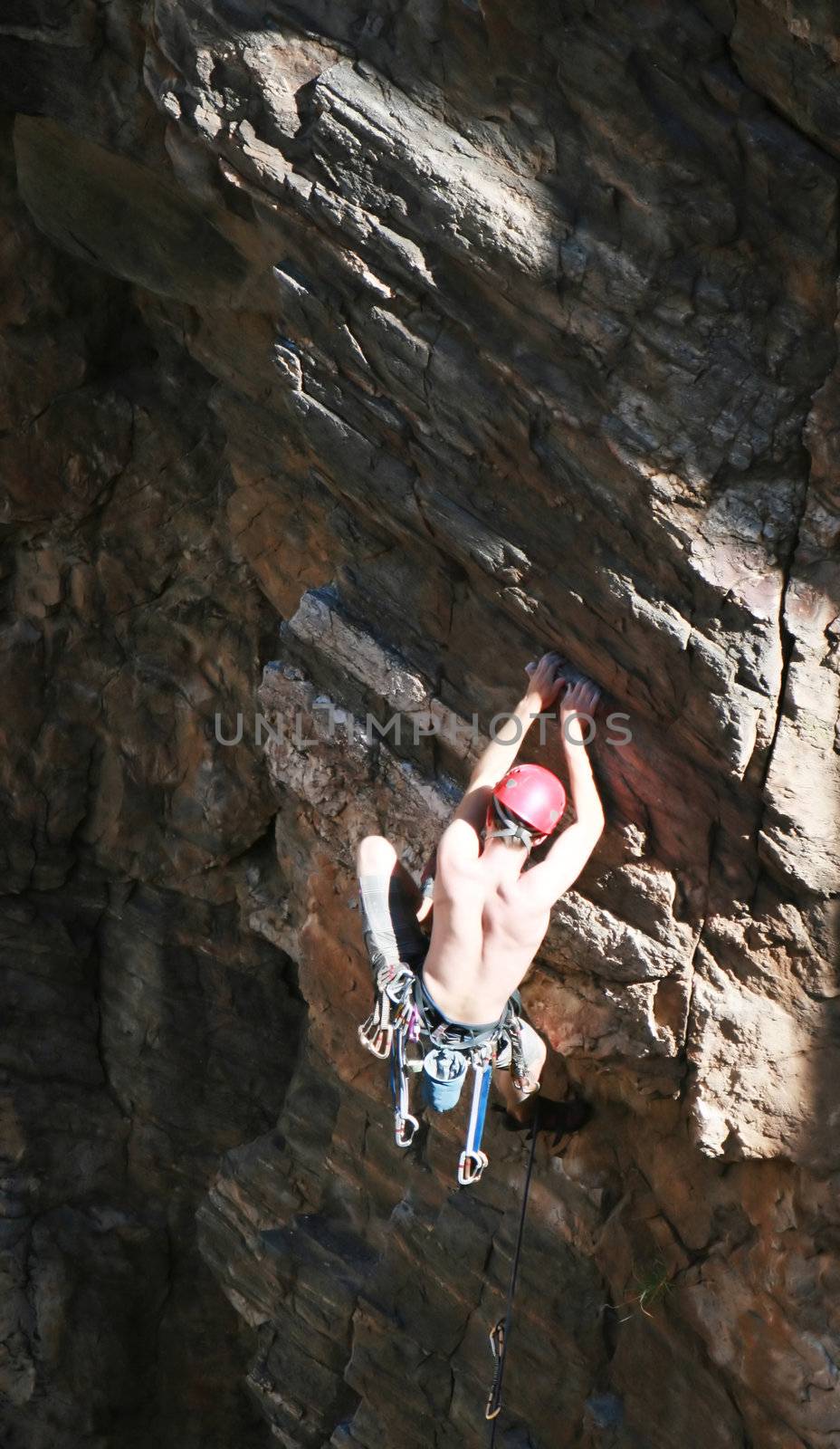 A rock climber works his way up a rock face protected by a rope clipped into bolts. He is wearing a helmet and quickdraws dangle from his harness. The route is in the desert southwest United States. Mt Lemmon, Arizona.