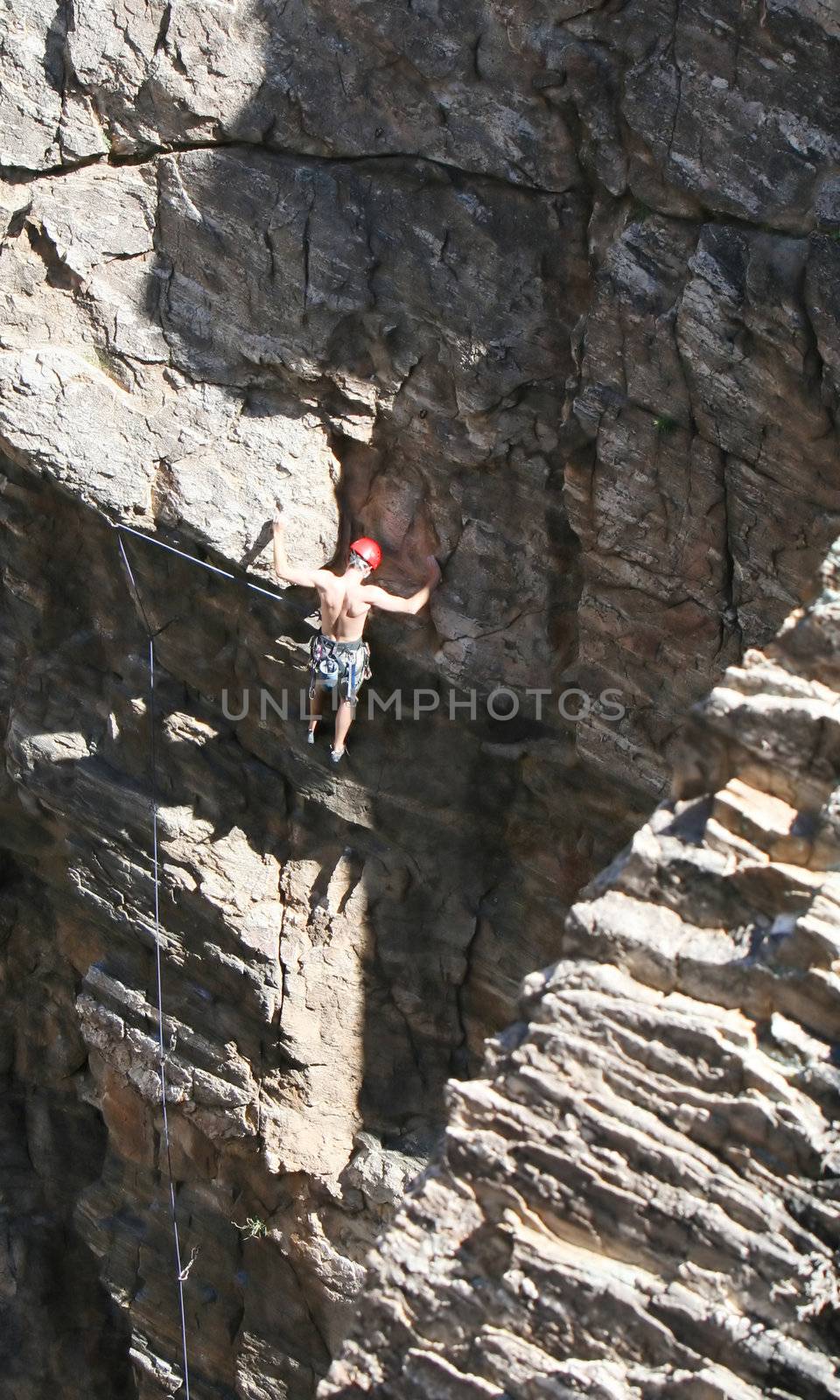 A rock climber works his way up a rock face protected by a rope clipped into bolts. He is wearing a helmet and quickdraws dangle from his harness. The route is in the desert southwest United States. Mt Lemmon, Arizona.