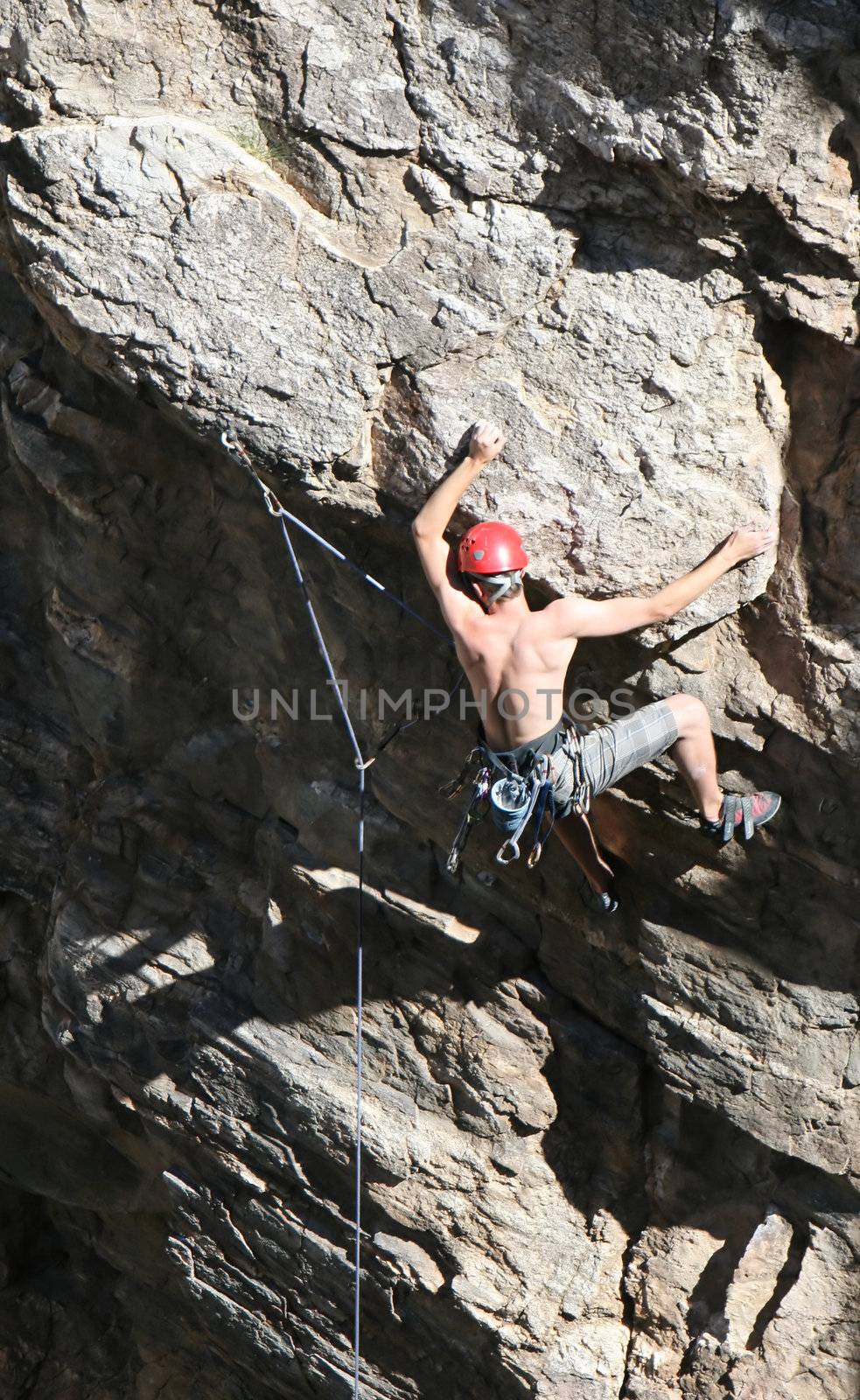 A rock climber works his way up a rock face protected by a rope clipped into bolts. He is wearing a helmet and quickdraws dangle from his harness. The route is in the desert southwest United States. Mt Lemmon, Arizona.