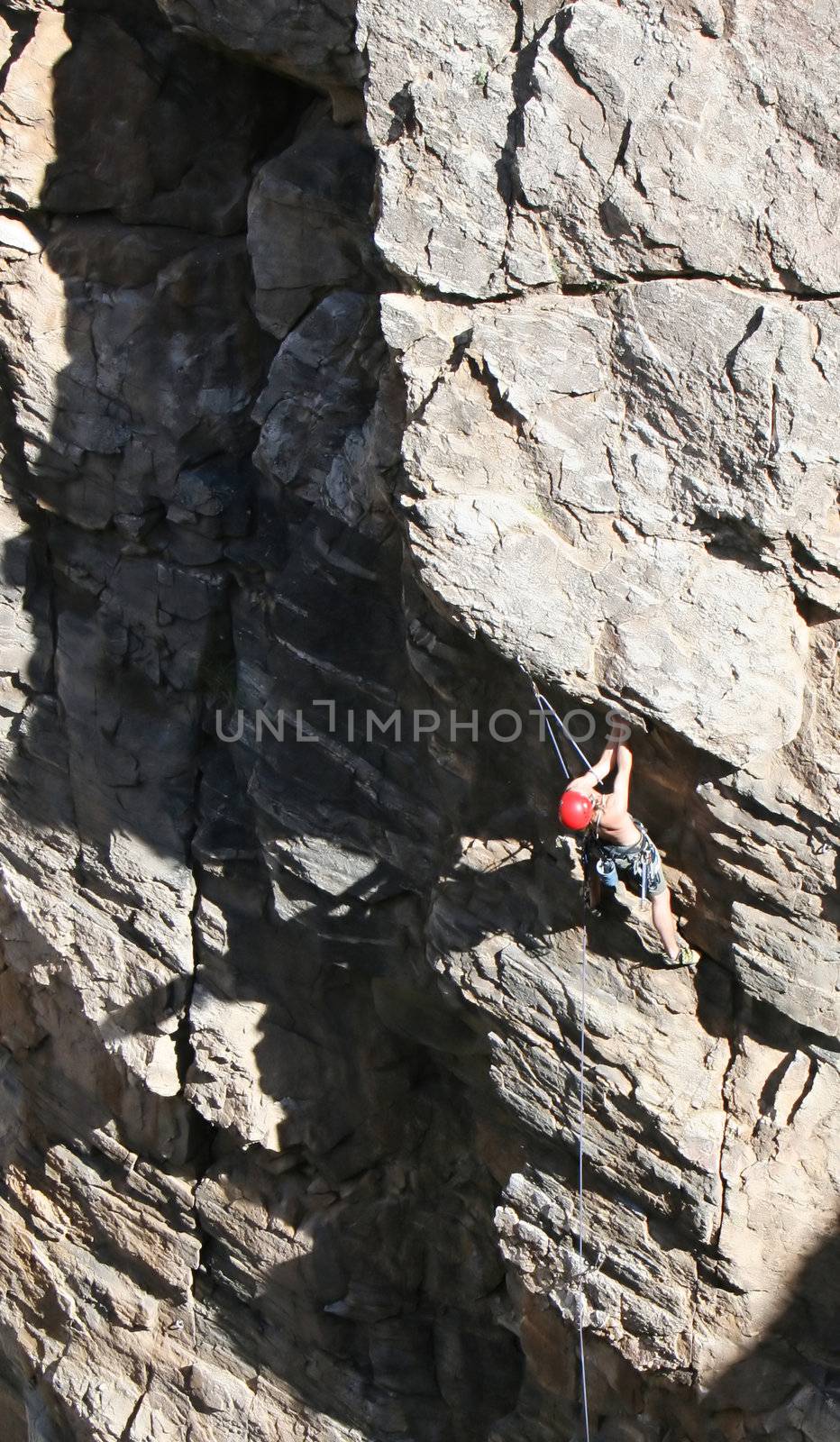 A rock climber works his way up a rock face protected by a rope clipped into bolts. He is wearing a helmet and quickdraws dangle from his harness. The route is in the desert southwest United States. Mt Lemmon, Arizona.