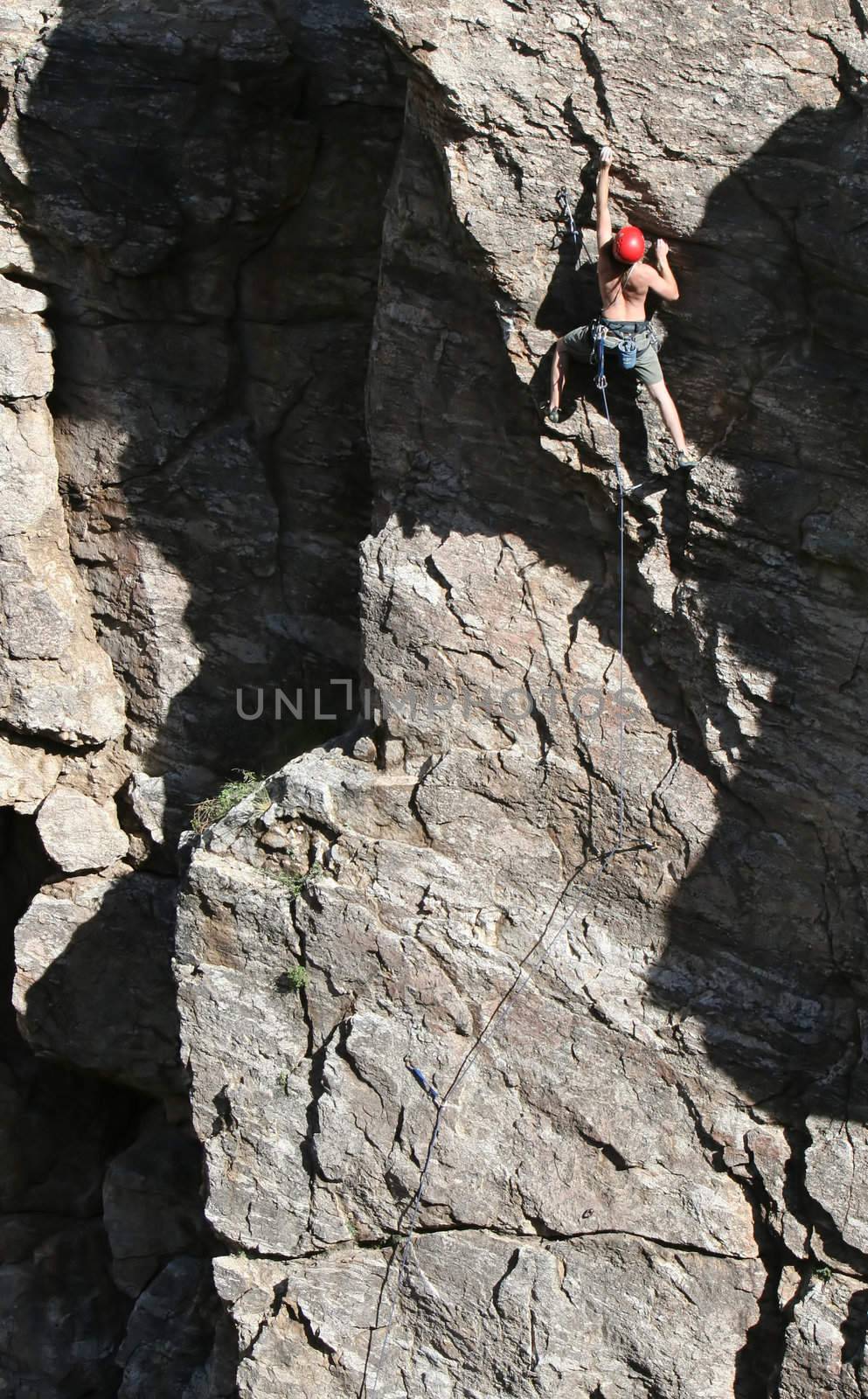 A rock climber works his way up a rock face protected by a rope clipped into bolts. He is wearing a helmet and quickdraws dangle from his harness. The route is in the desert southwest United States. Mt Lemmon, Arizona.