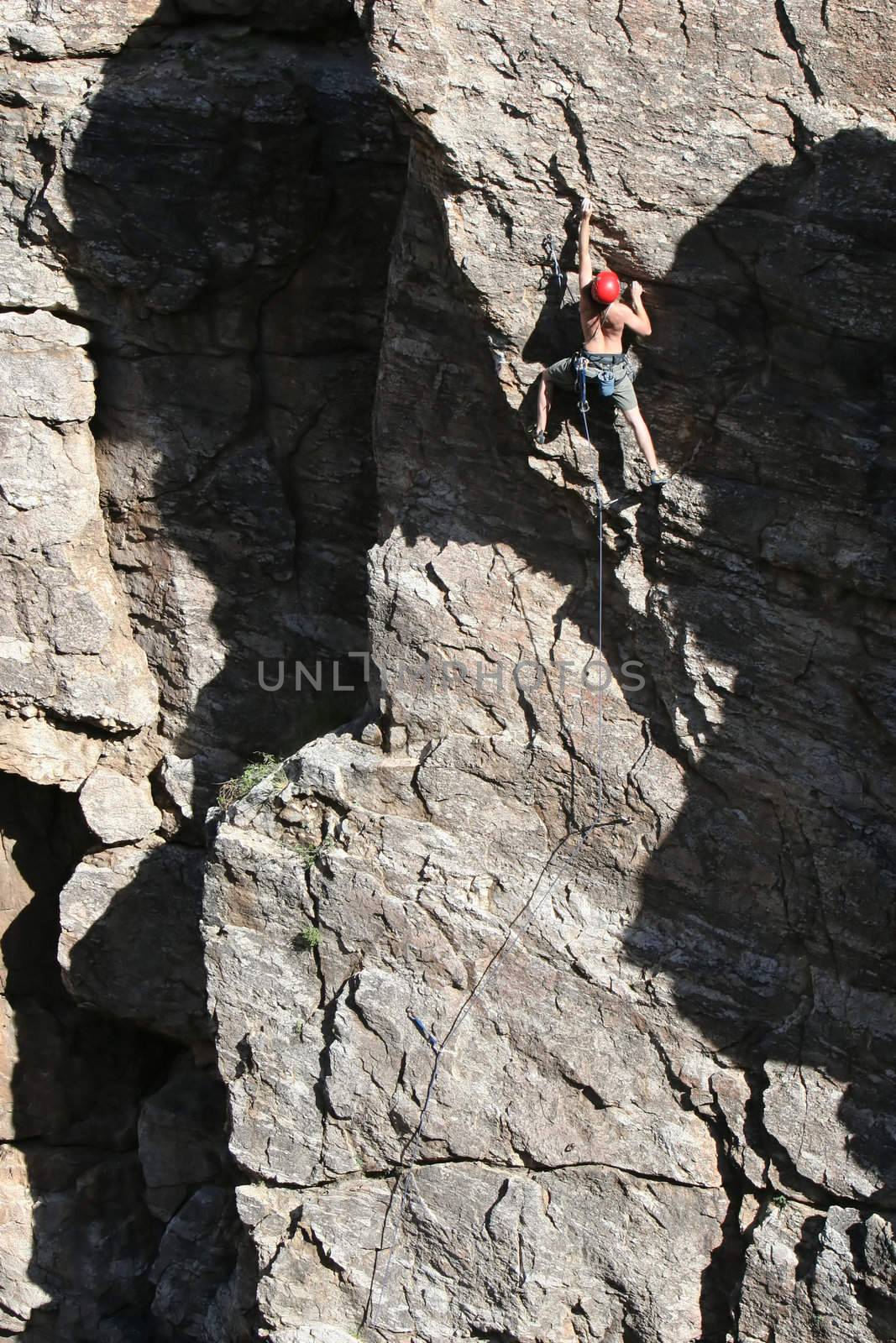 A rock climber works his way up a rock face protected by a rope clipped into bolts. He is wearing a helmet and quickdraws dangle from his harness. The route is in the desert southwest United States. Mt Lemmon, Arizona.