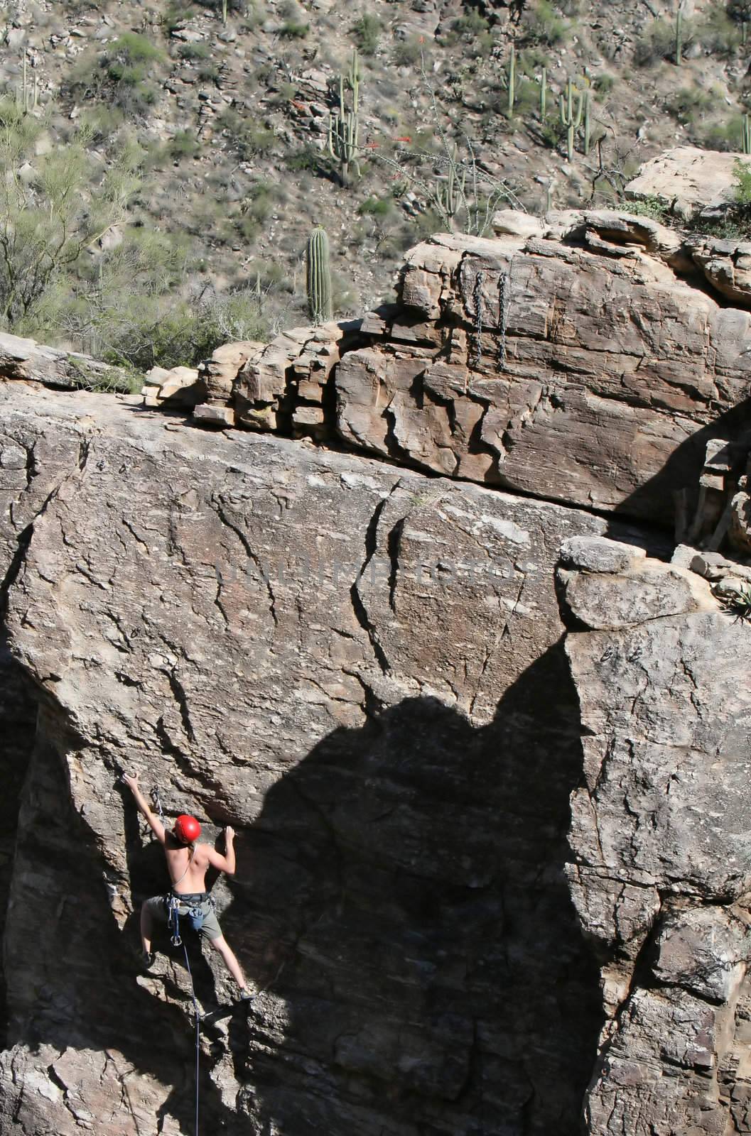 A rock climber works his way up a rock face protected by a rope clipped into bolts. He is wearing a helmet and quickdraws dangle from his harness. The route is in the desert southwest United States. Mt Lemmon, Arizona.