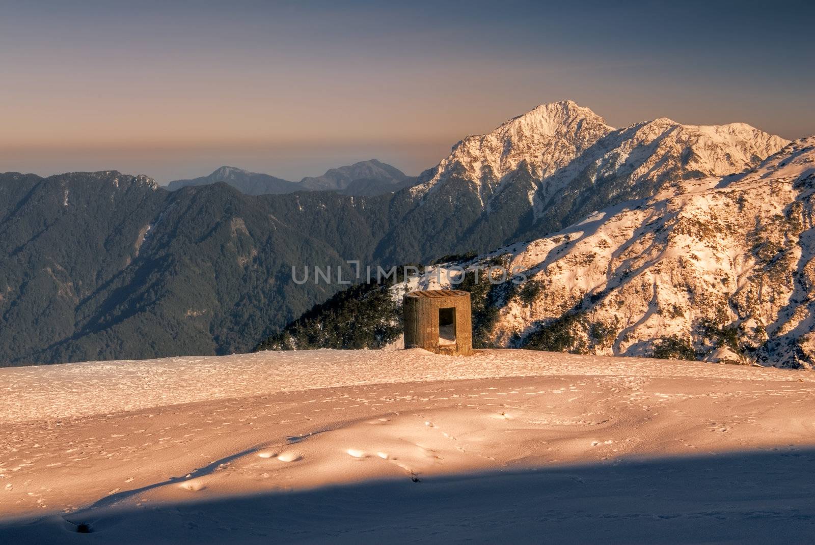 Beauty of snow mountain with blockhouse in yellow sunset.