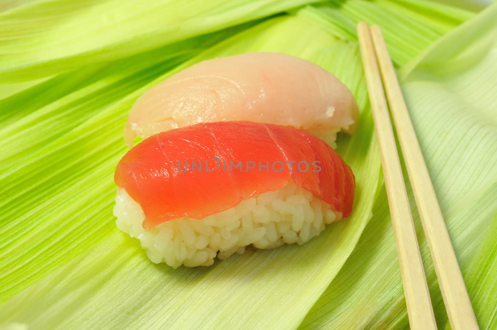 close up traditional fresh japanese sushi on green leafs with wooden chopsticks, focus on front piece