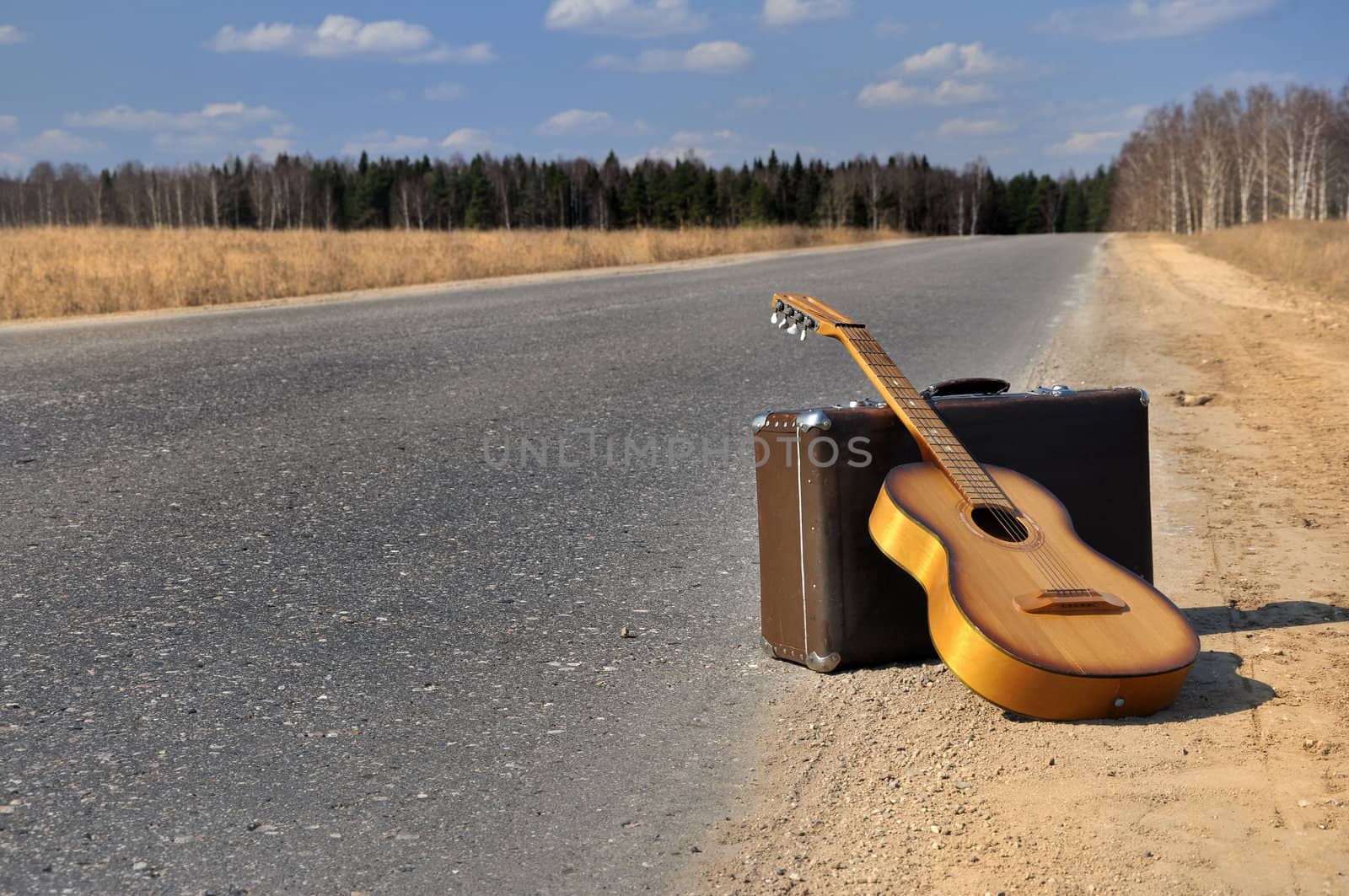 baggage and guitar lies on empty countryside road