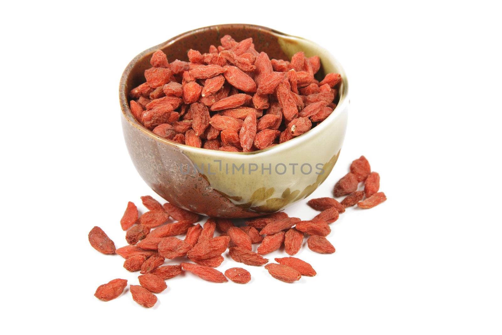 Red dry goji berries in a small green and brown dish on a reflective white background