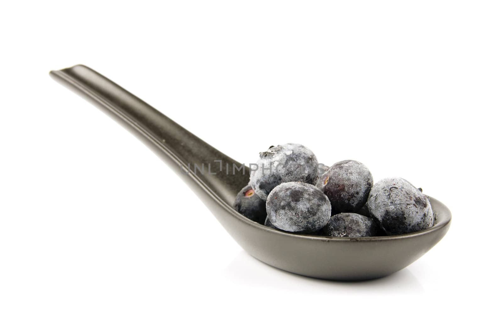 Blue ripe blueberries on s amll black spoon with a reflective white background