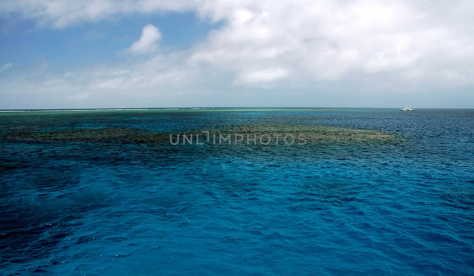 blue calm sea, coral reef, small white boat in background