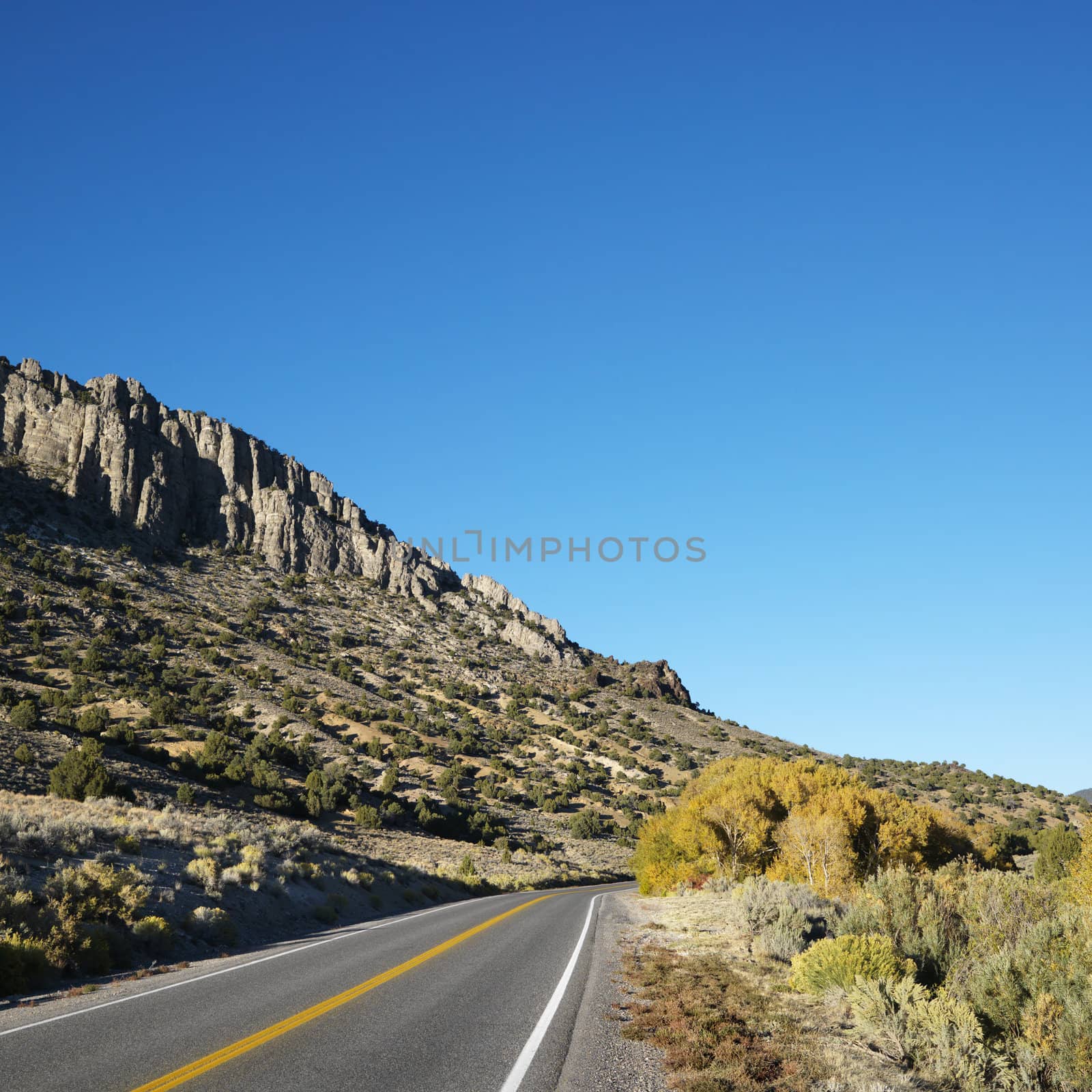 Strip of highway cutting through montain range under clear blue sky.