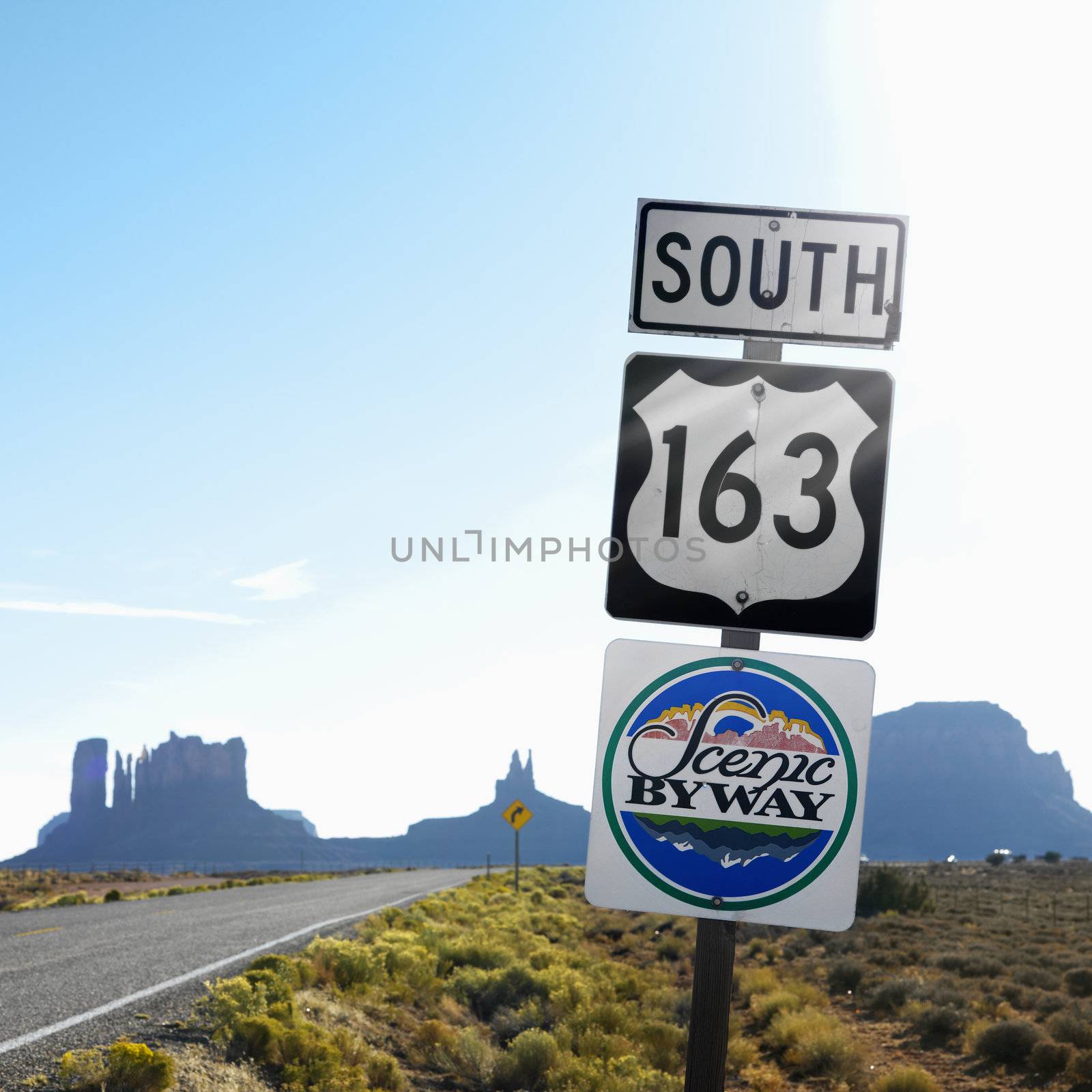 Sign for Scenic Byway 163 south beside road with rock formations in background in Monument Valley, Utah.