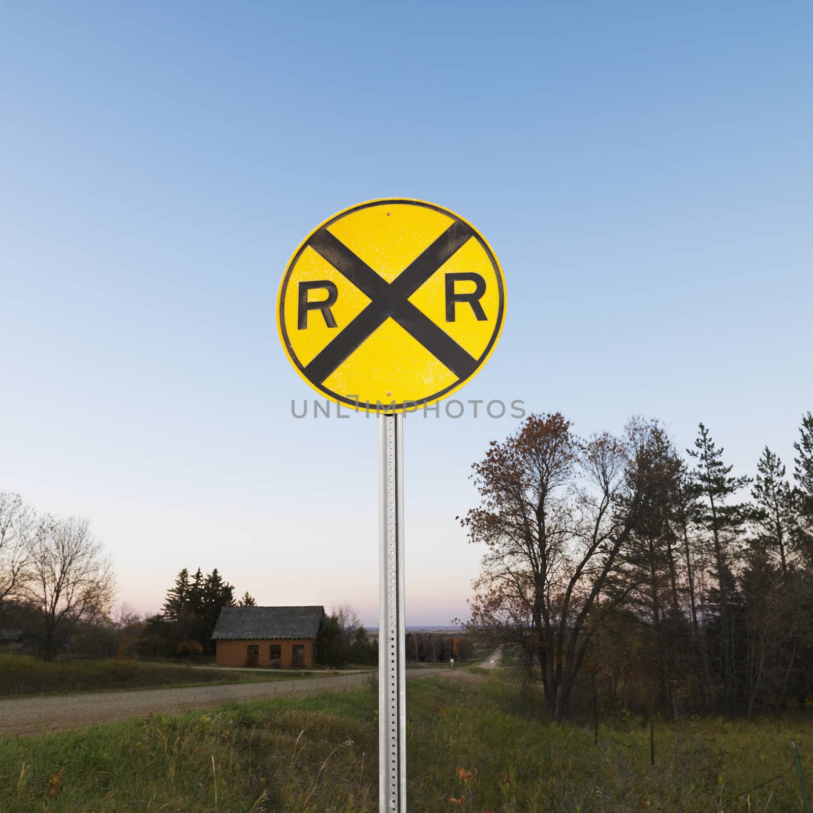 Circular yellow railroad grade crossing sign in rural setting.