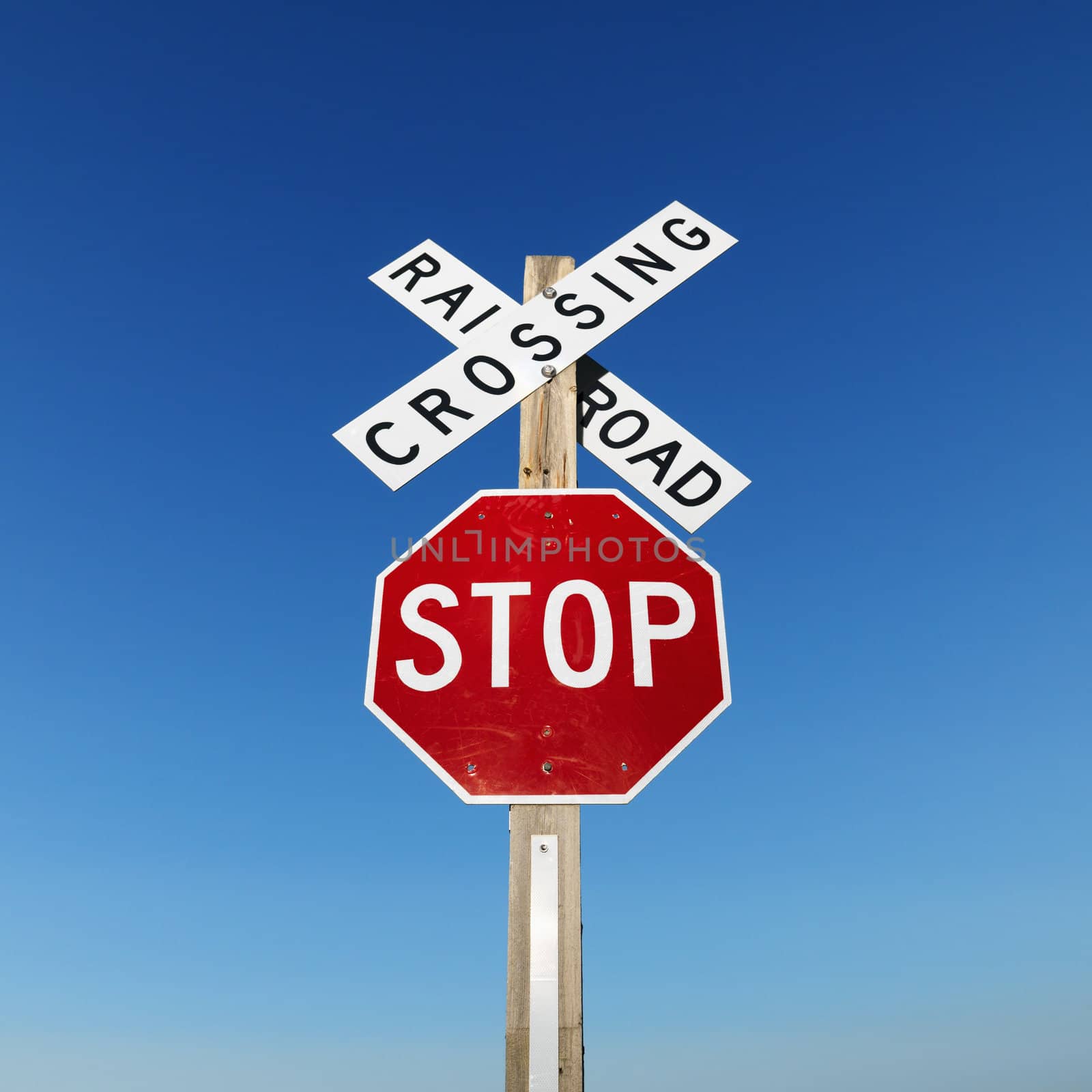Railroad crossing and stop signs against blue sky.