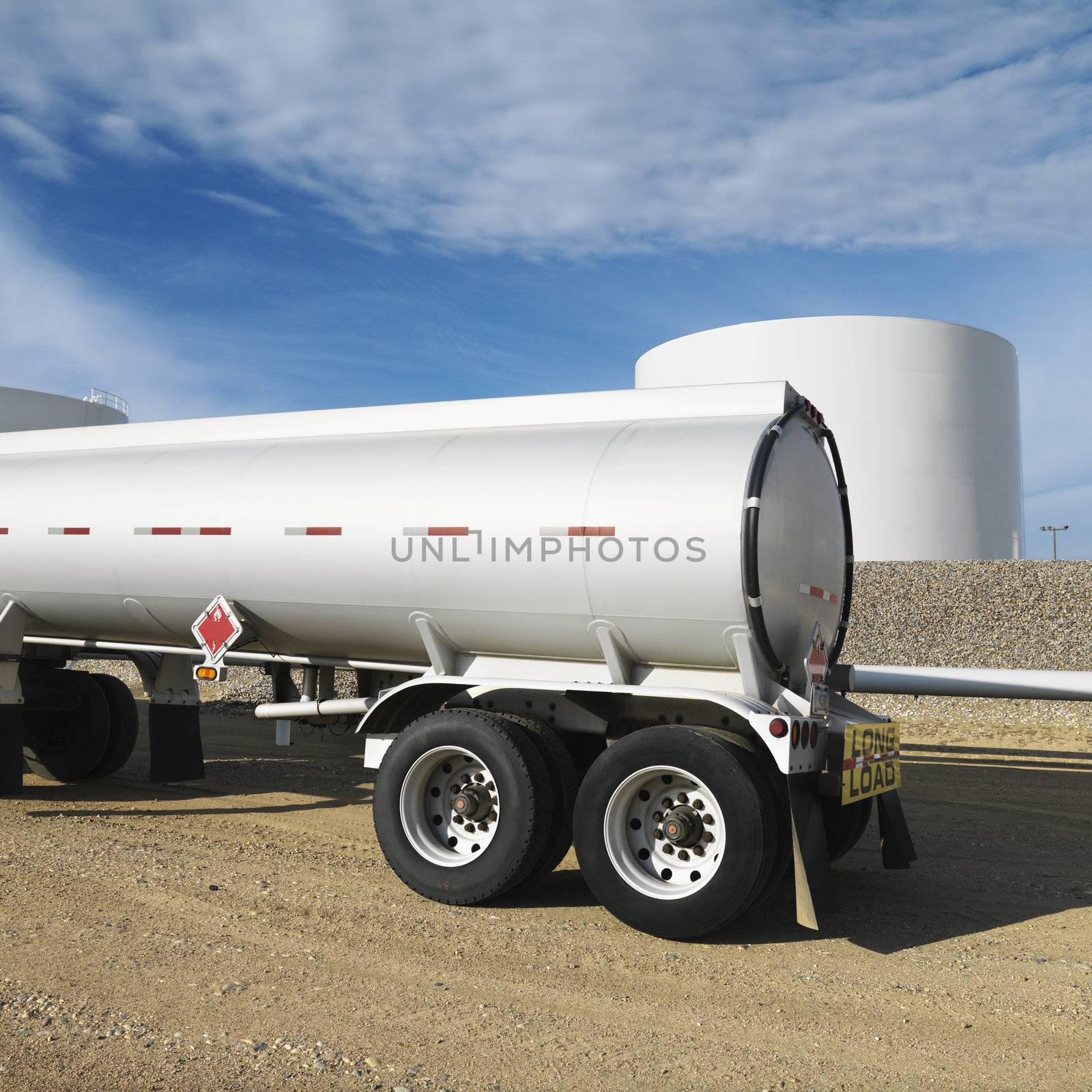 Side view of fuel tanker truck with fuel tank farm in background.