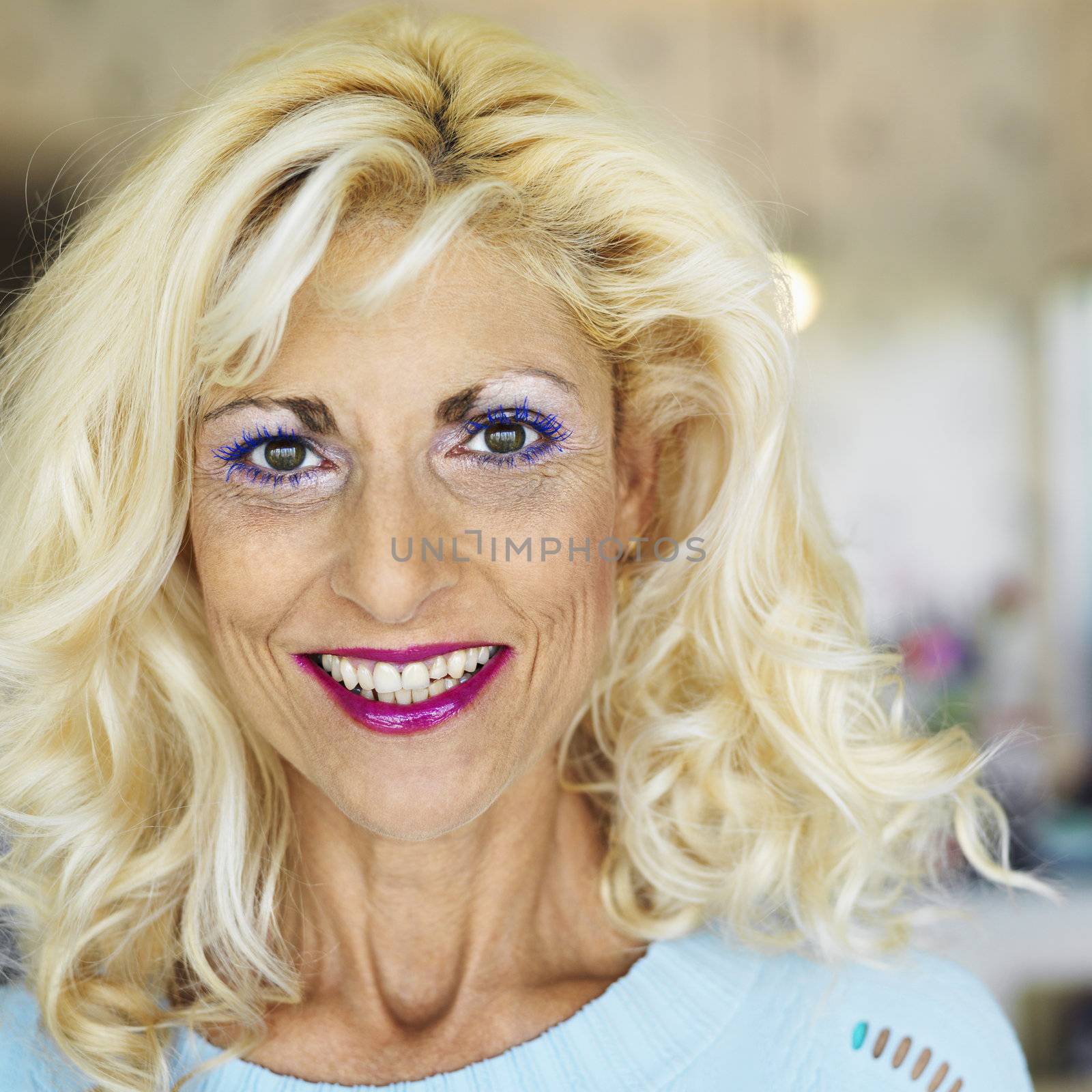 Portrait of tan blonde Caucasion middle-aged woman wearing lots of makeup smiling at viewer.