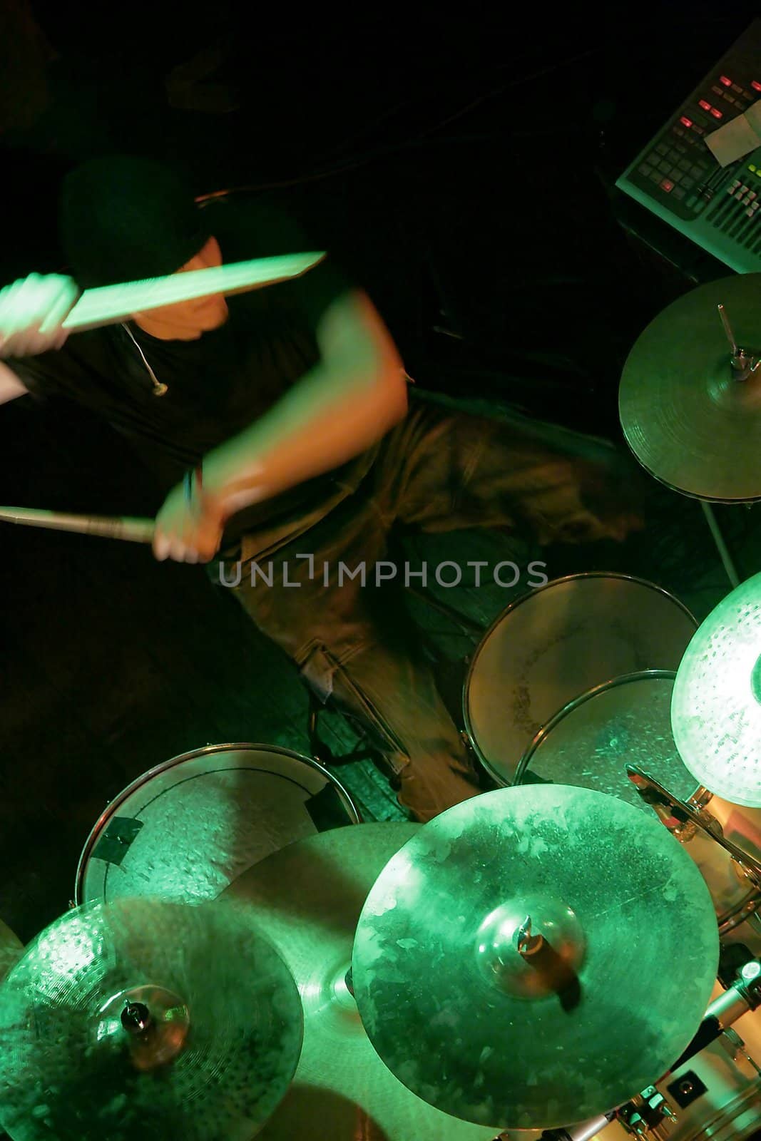 drummer in shadow playing on drums illuminated with green light, drummer is in motion, drumsticks blurred