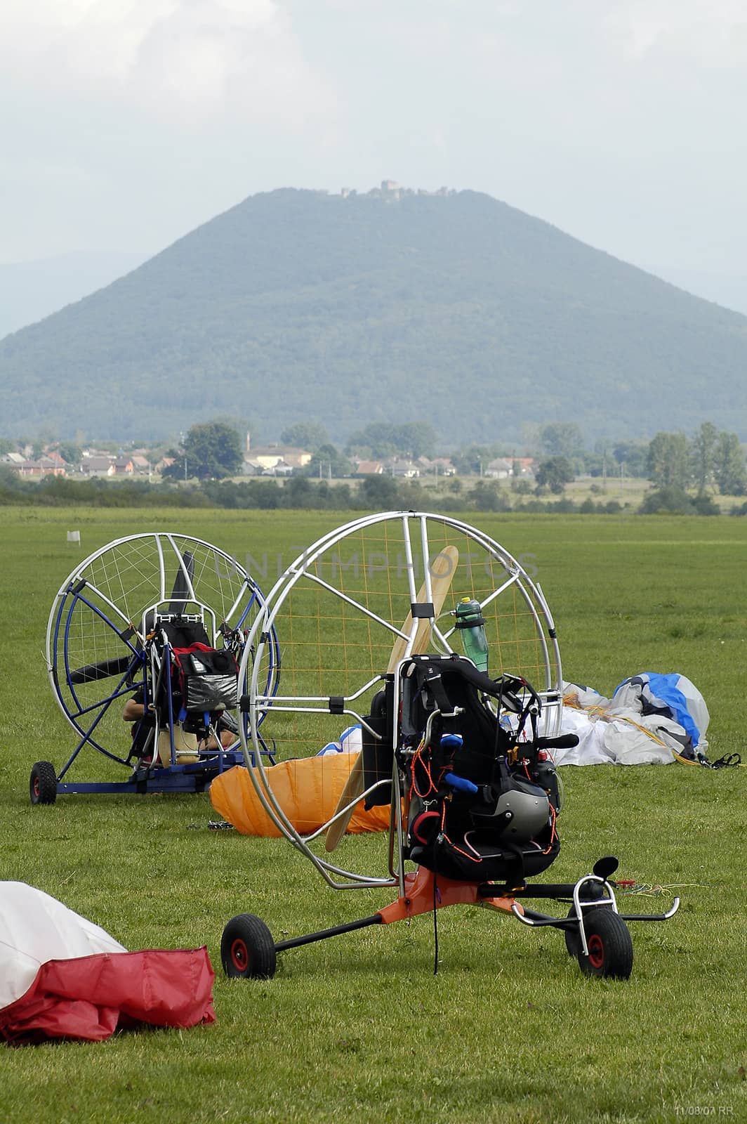 two empty paragliding machines, parachutes, big hill with castle in background