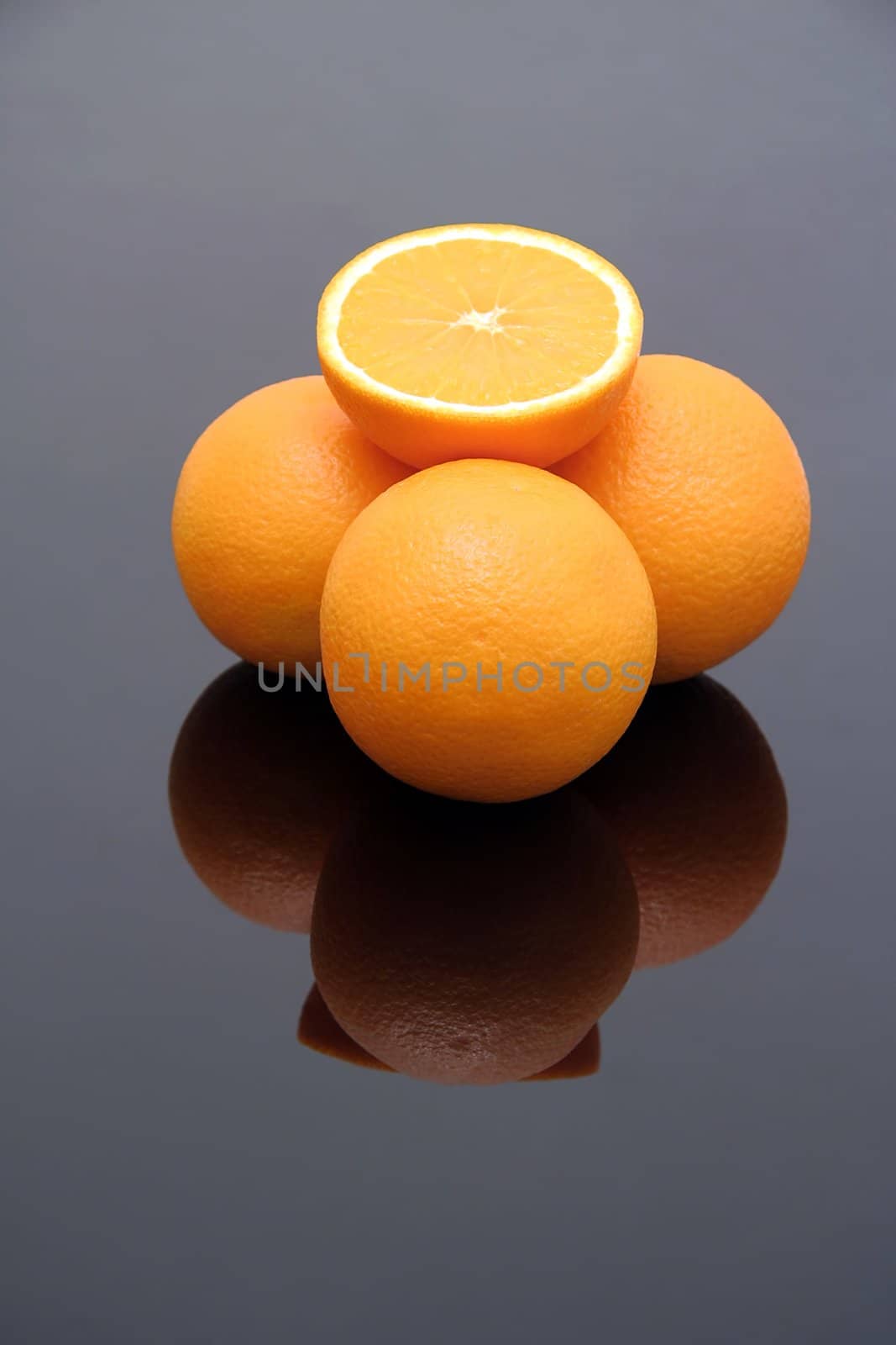 fresh oranges on reflective background, one is cut in half