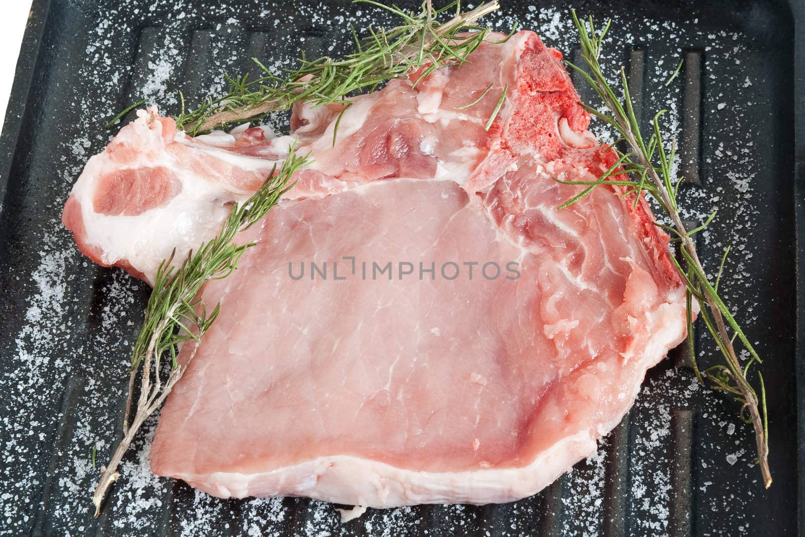 raw pork chop on a griddle with salt and rosemary ready to be cooked
