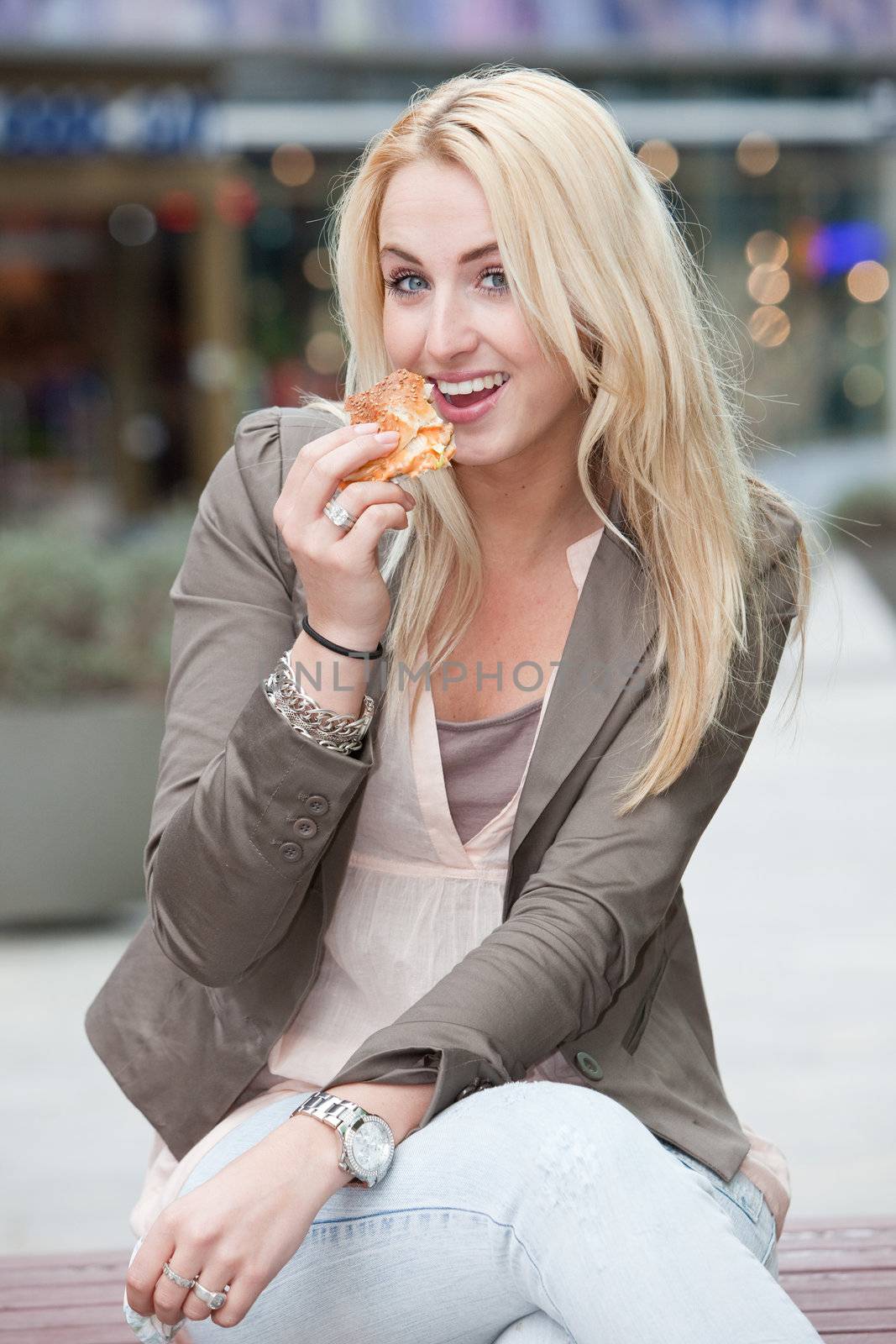 Beautiful young blond girl eating a hamburger and looking happy