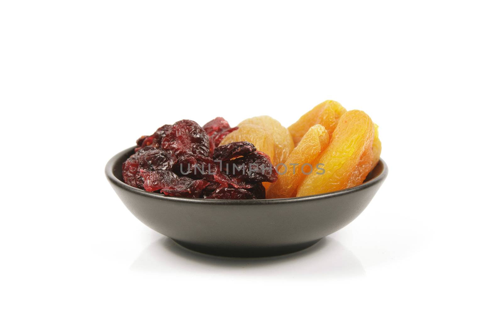 Red ripe dried cranberries and dried apricots in a small black bowl on a reflective white background