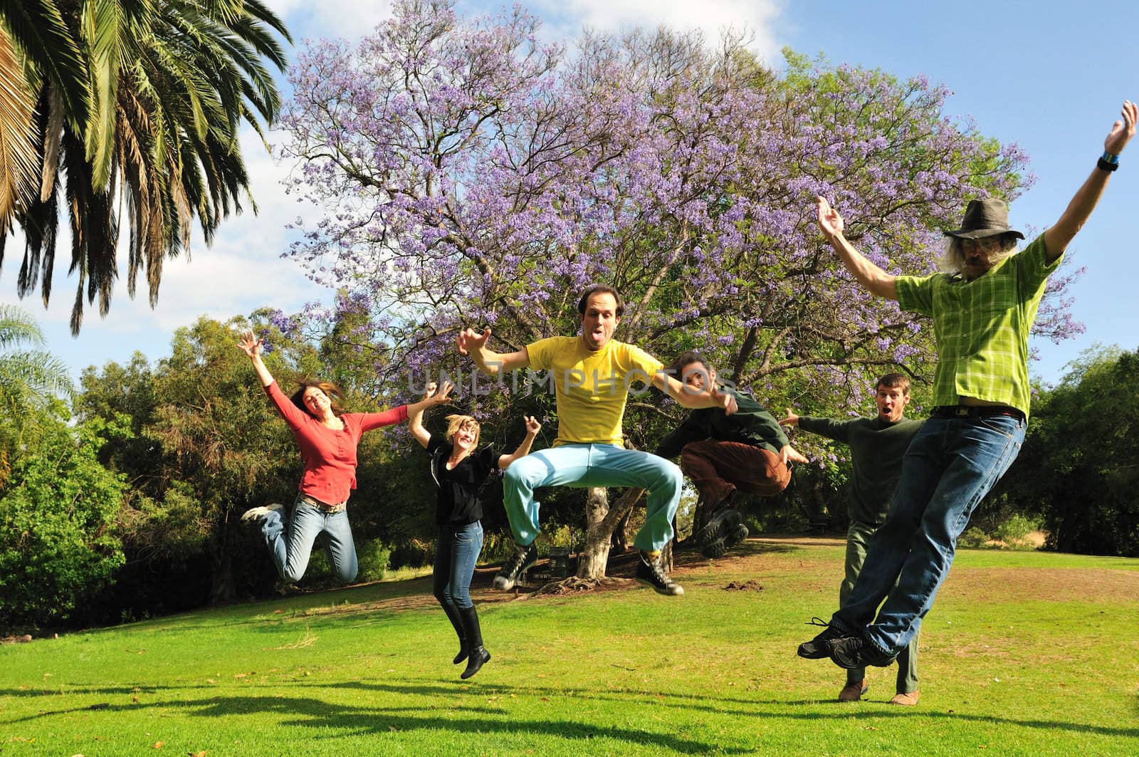 Group of six silly adults jump into the air with joyful enthusiasm