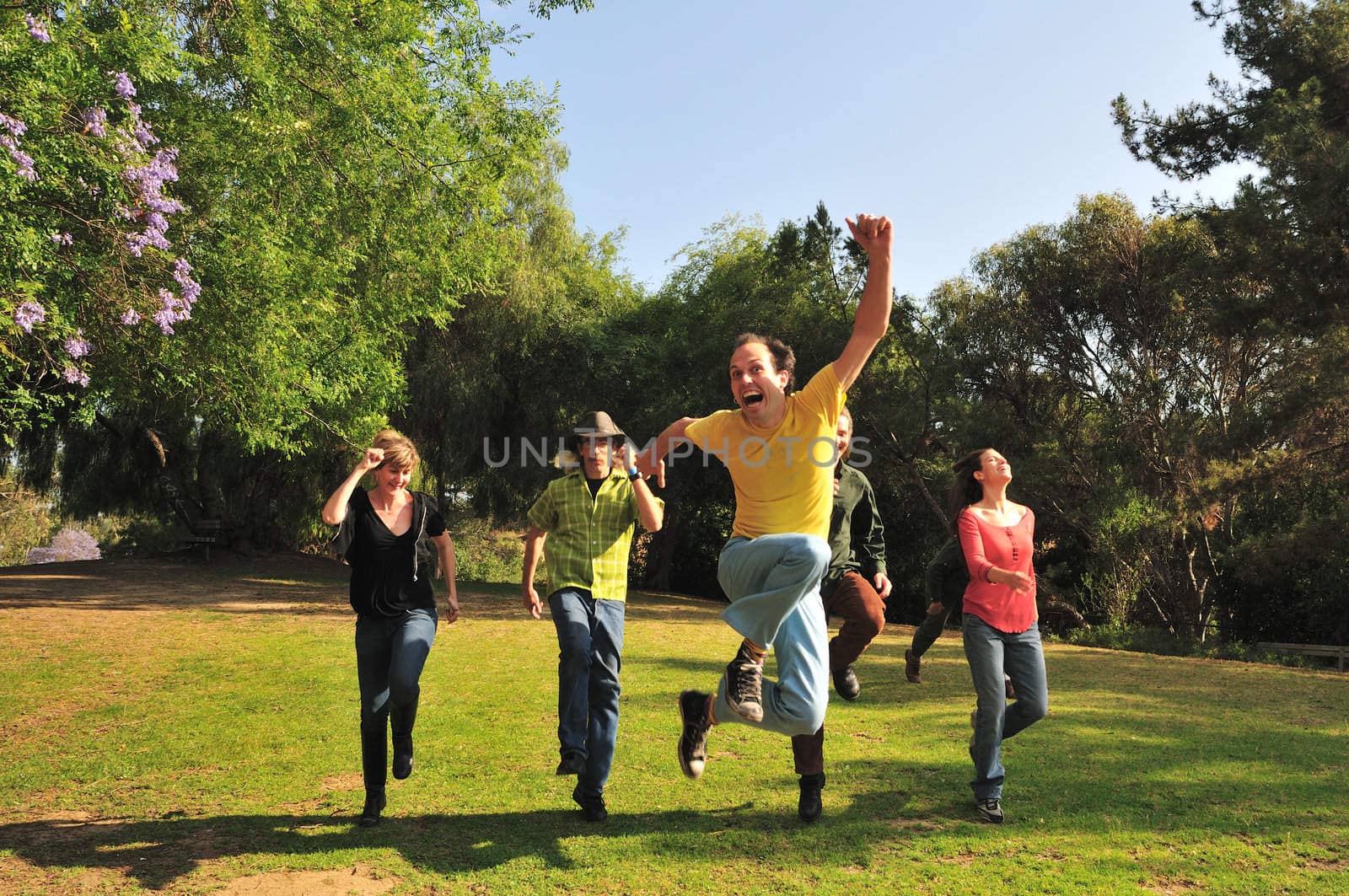 Group of six friends skipping through a park in the summer