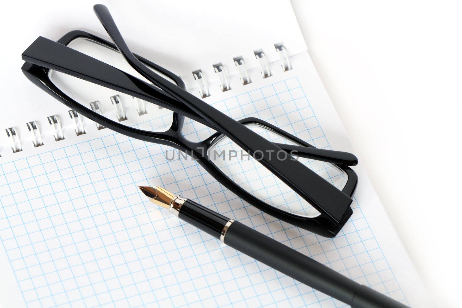 Closeup of fountain pen and  black spectacles lying on open spiral notebook