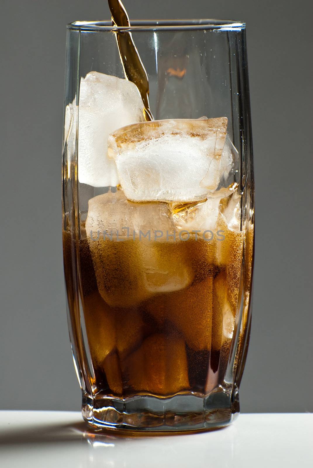 Cola being poured into a glass that is filled with ice cubes