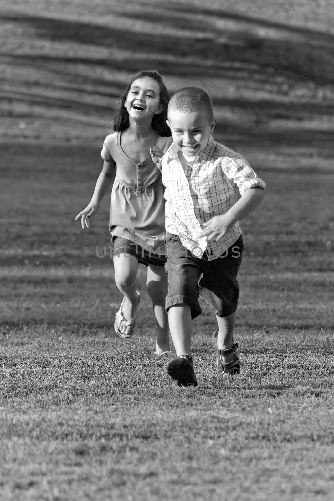 A little boy and girl laughing and running through the grassy field in black and white.