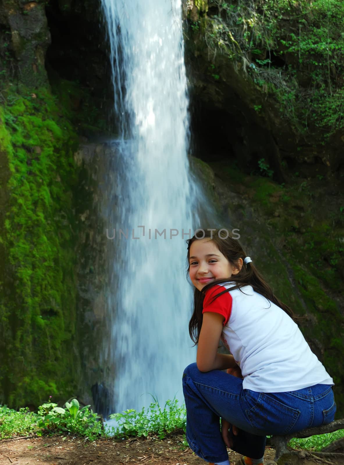 a beautiful little girl is sitting beside a waterfall