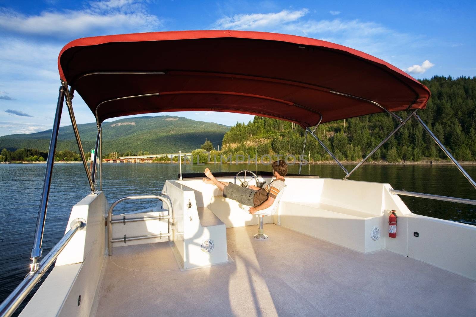 A young male driving a house boat from the upper helm.