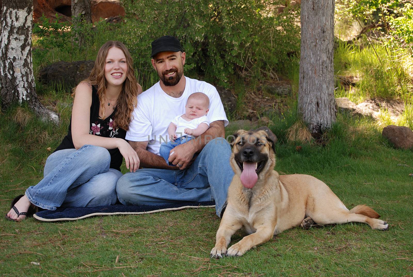 Horizontal image of a young modern family of three and their dog resting in the park.
