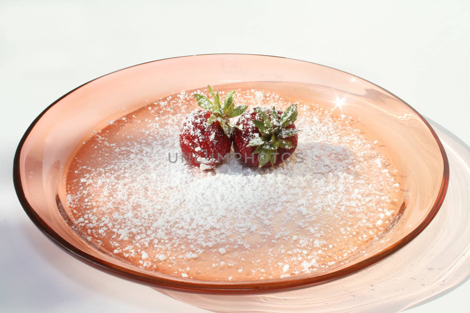 Two strawberries with powdered sugar on pink plate against a white background