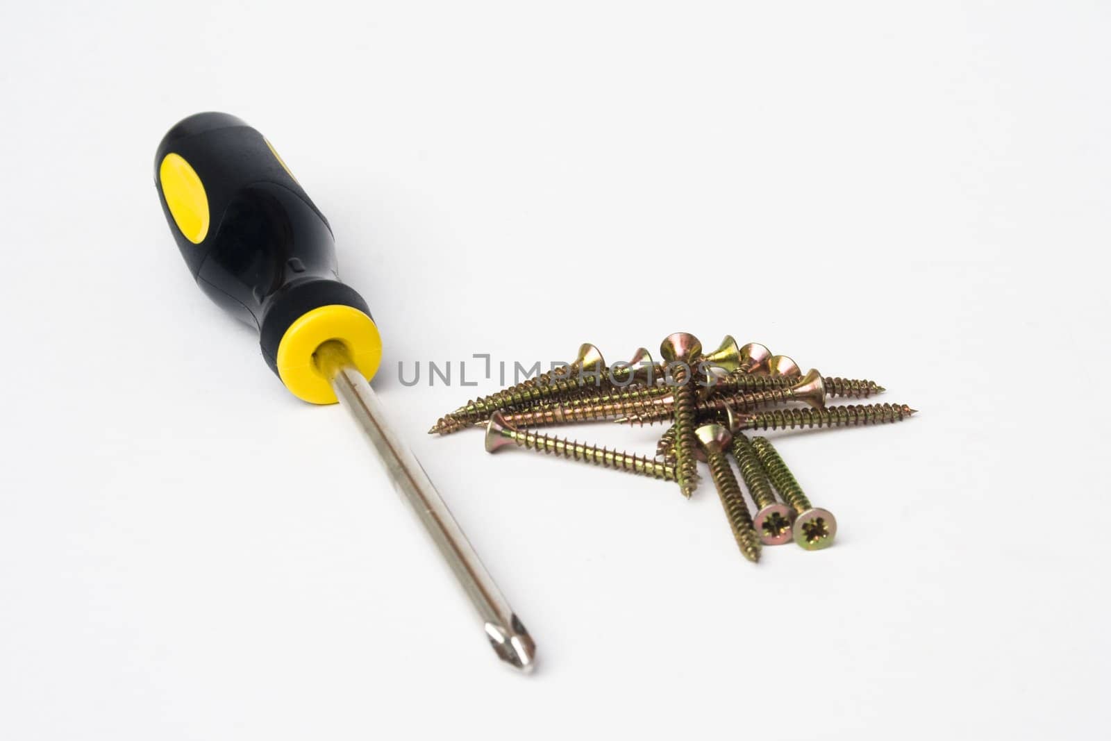 Yellow and black handled phillips screwdriver with pile of scews on white background