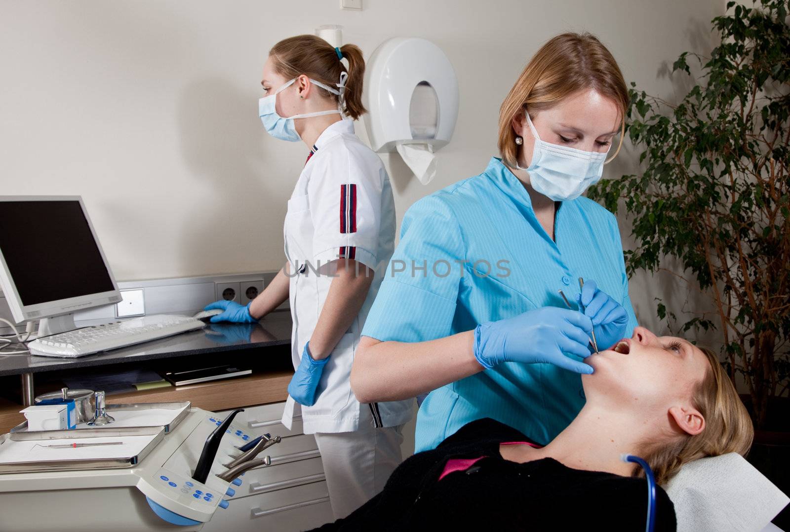 Female dentist working on her patient with assistant in the background