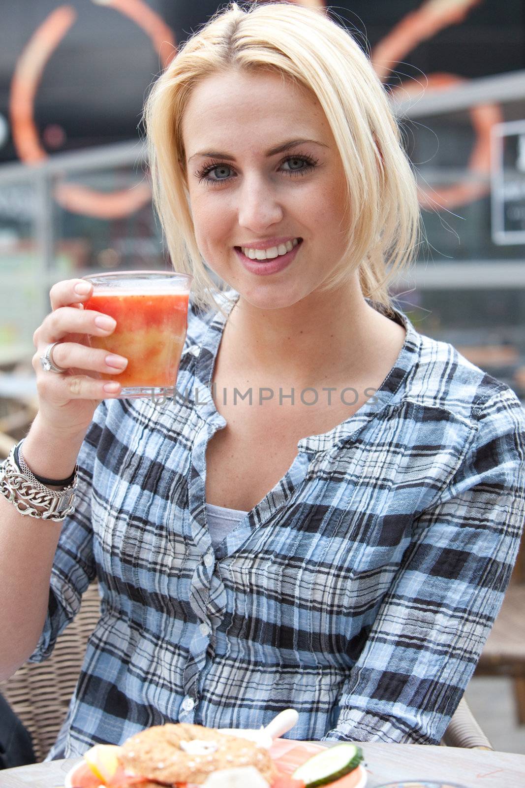 Attractive young woman drinking a healthy glass of juice outside on a terrace