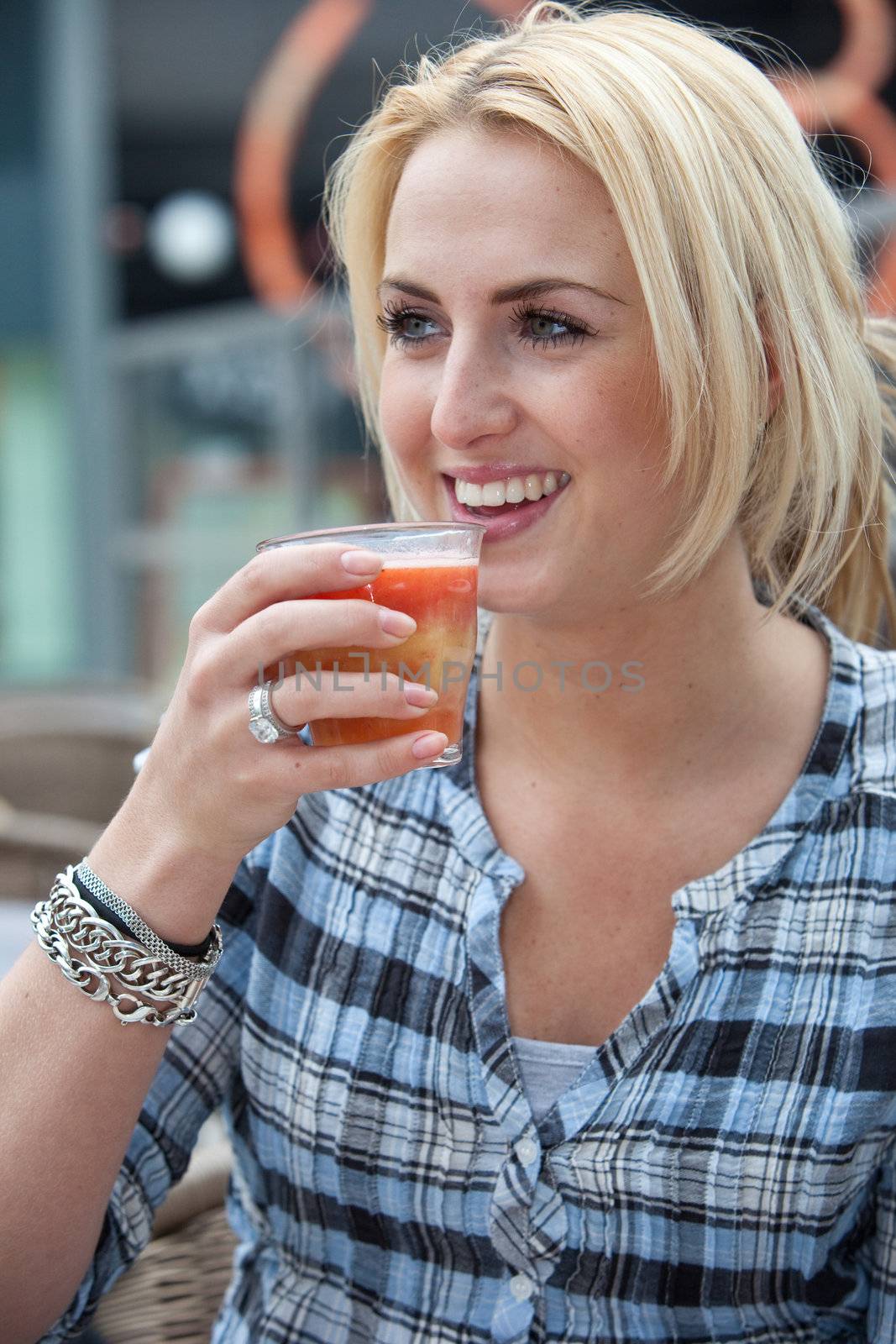 Beautiful young woman drinking a glass of healthy juice outdoors on a terrace