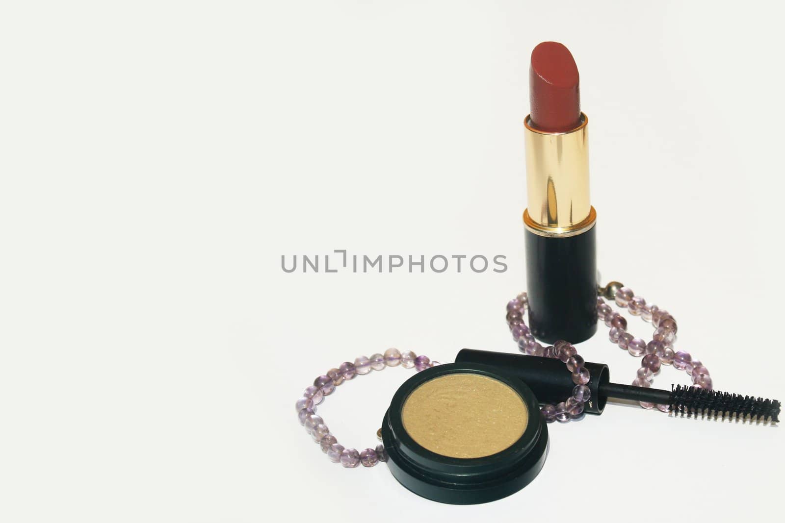 Lipstick, mascara, eyeshadow and a necklace on white background with copy space on left
