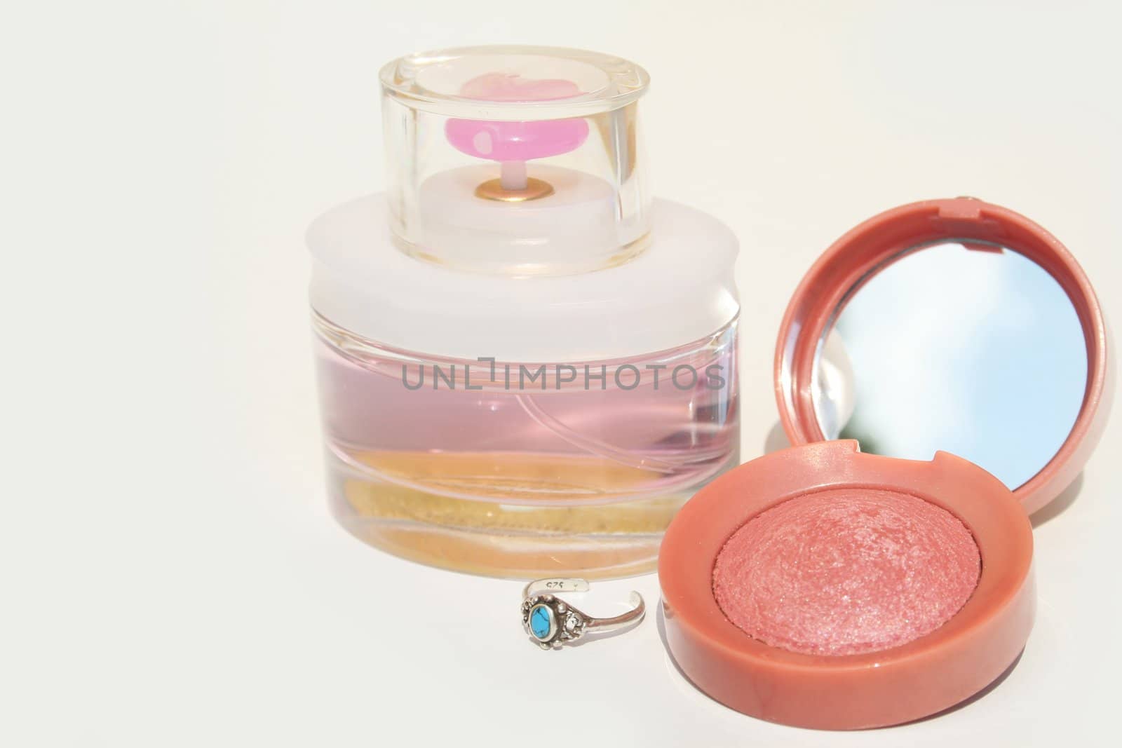 Perfume, blush and a blue stone ring on white background with copy space on left