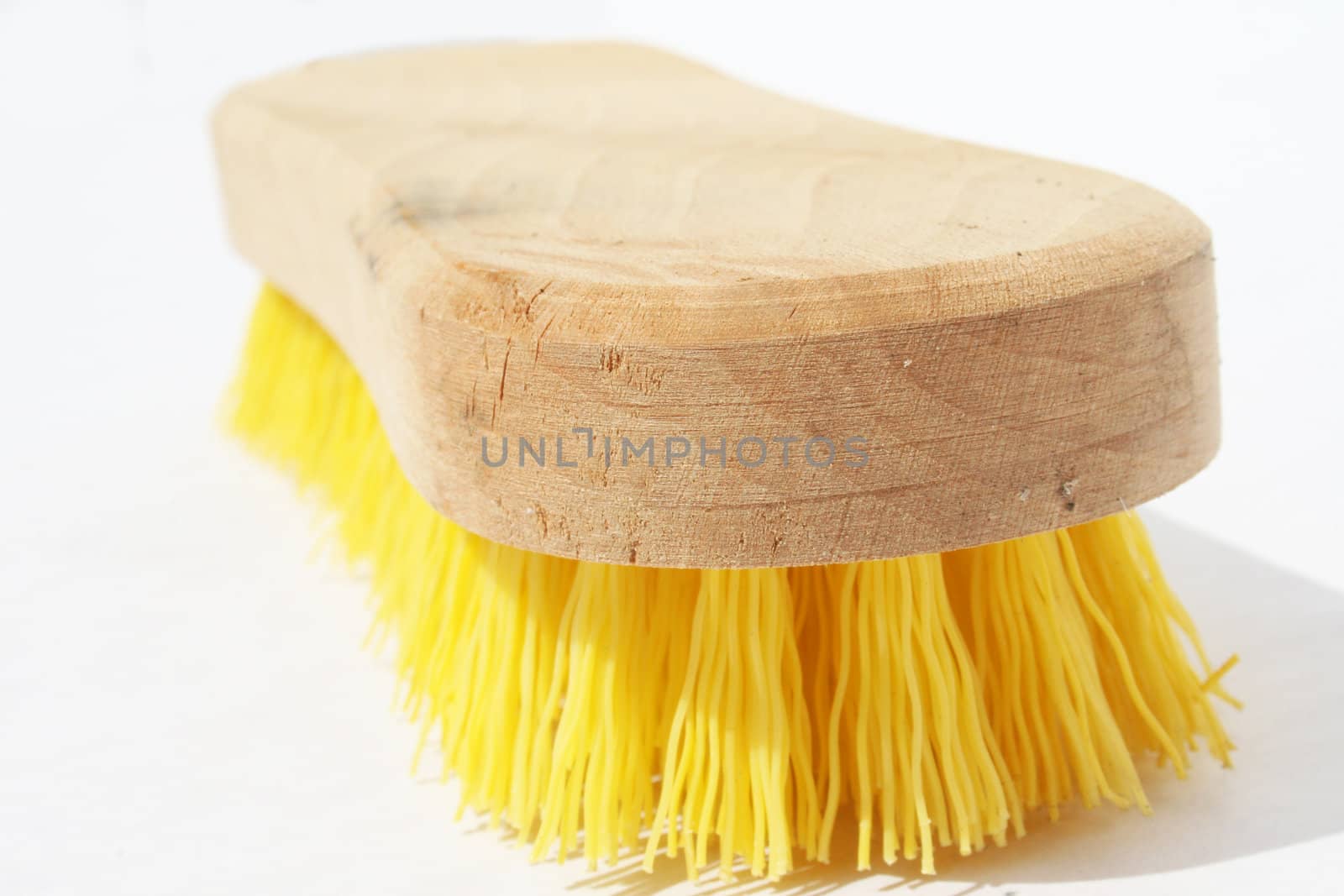 Scrub brush with polyester yellow bristles and wood handle against white background