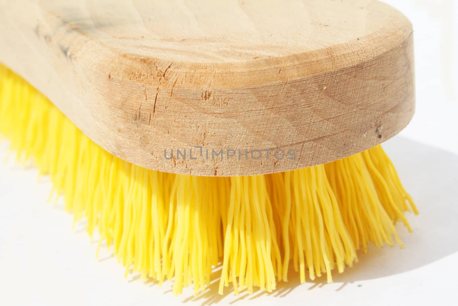 Scrub brush with polyester yellow bristles and wood handle against white background