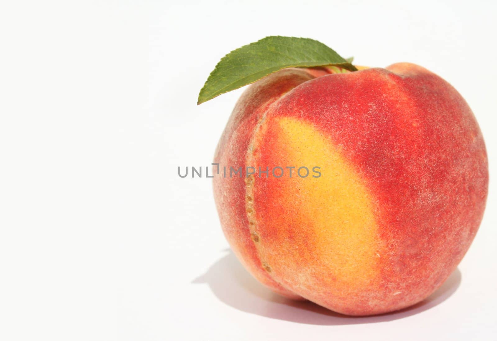 Single ripe peach with green leaves on white background