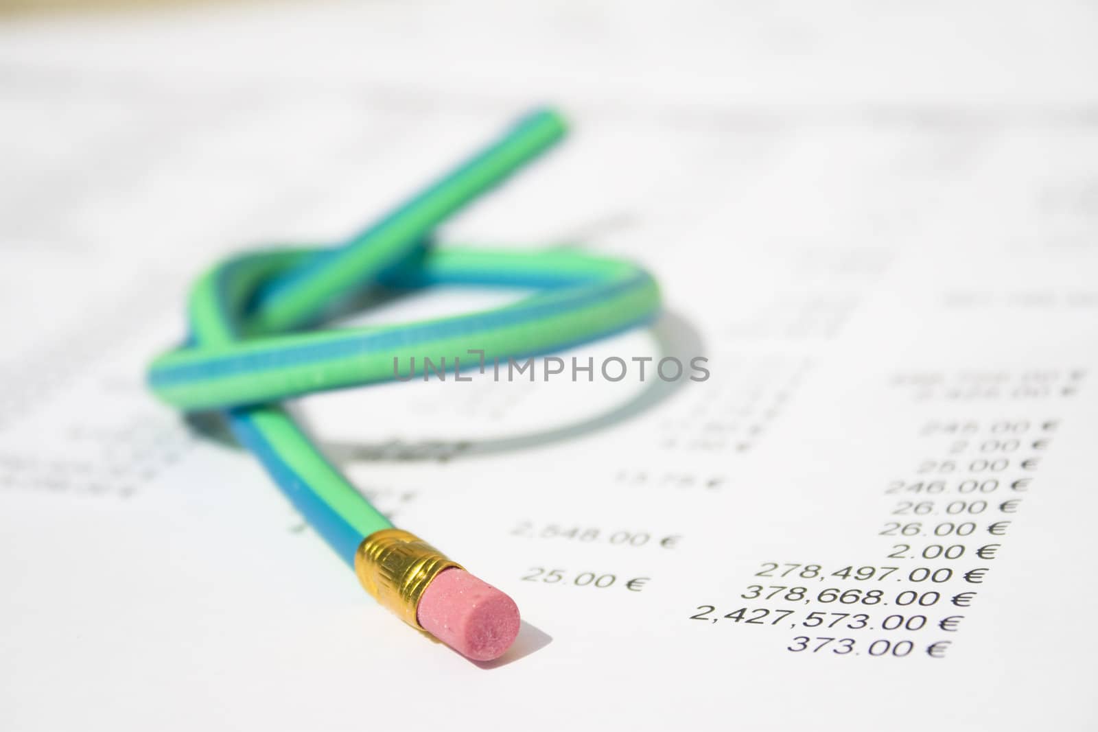 A green and blue striped rubber pencil tied in knot sitting on accounting printout