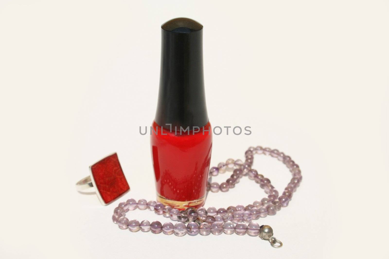 A bottle of red fingernail polish with purple beaded necklace and red ring 