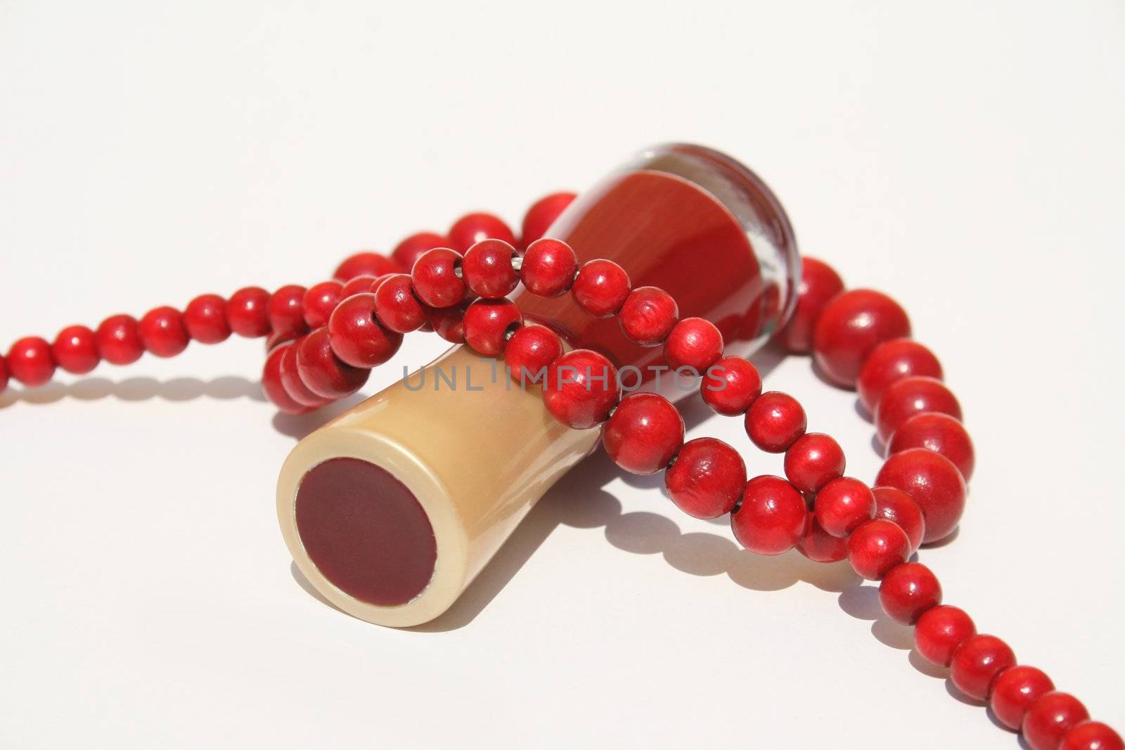 A bottle of red fingernail polish on side with strand of red wooden beaded necklace wrapped around